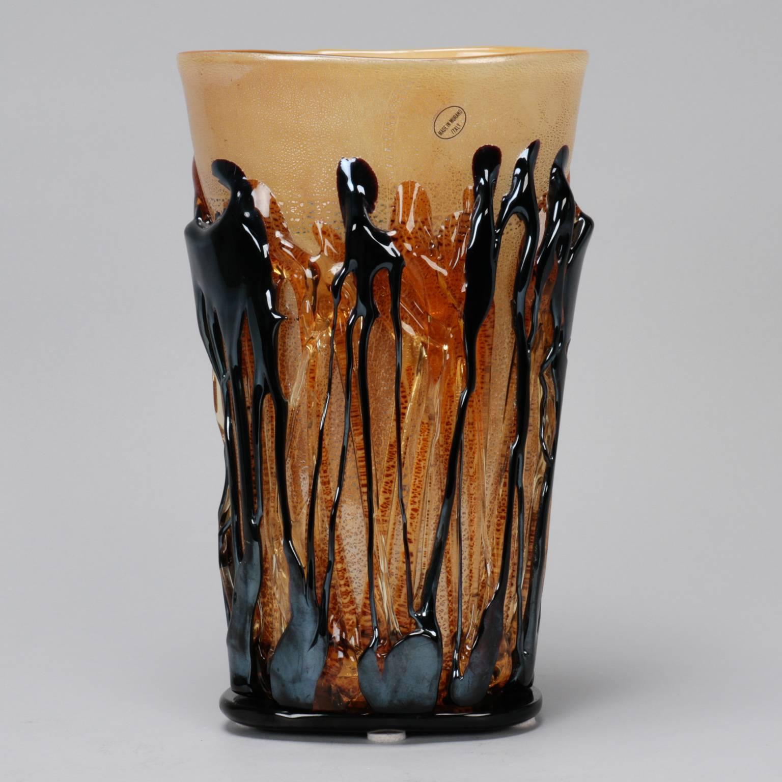 Creamy golden taupe colored Murano glass vase, circa 1990s with a subtly flared shape that stands just over 12” high. Base and body of vase are encased in applied black and amber glass strings. Original made in Murano Italy label affixed.