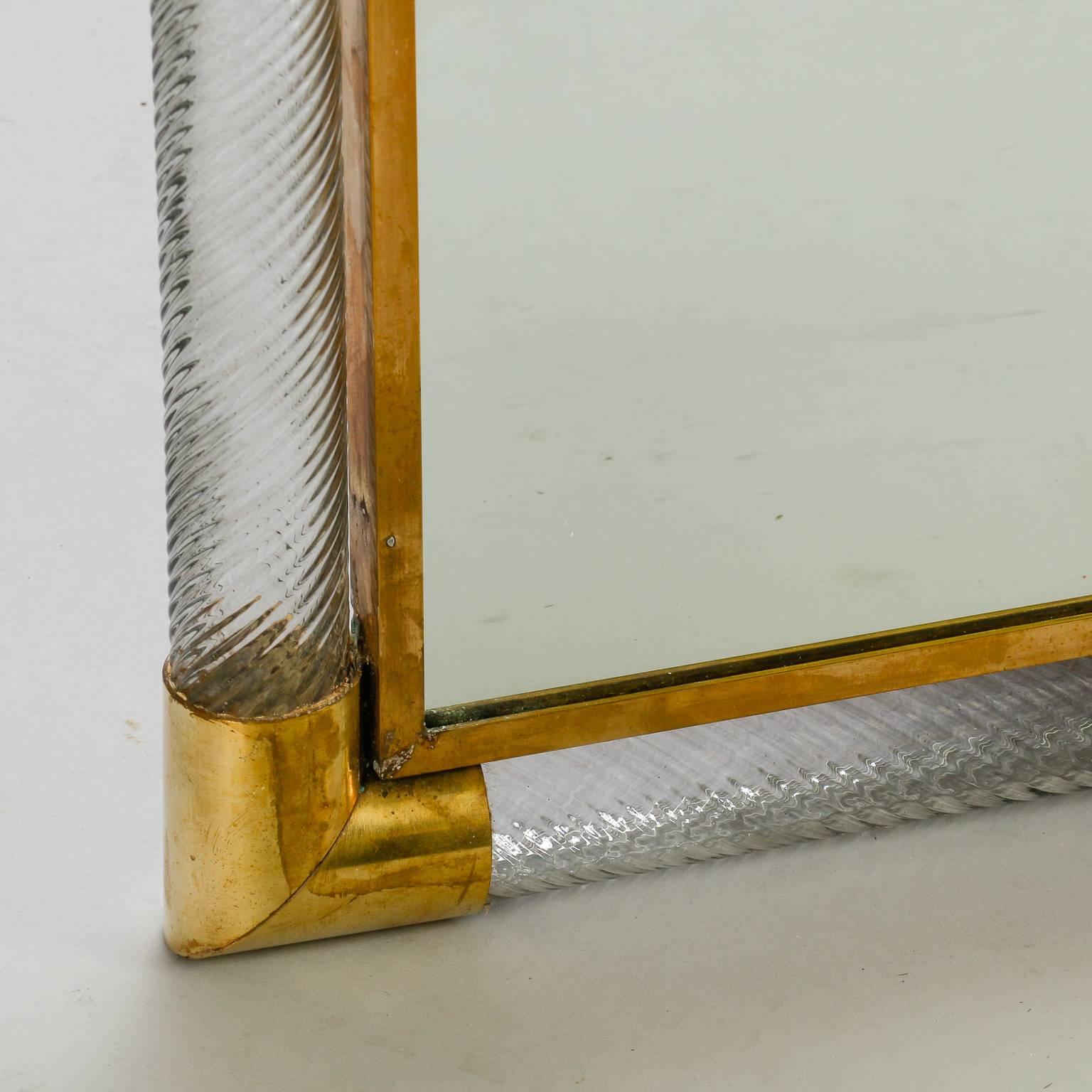 Mirror with Murano glass and brass frame, circa 1960s. Found in Italy, this mirrors is framed with thick, pale gray glass with ribbed and twisted surface with polished brass embellishments. Excellent vintage condition with no flaws found.
    