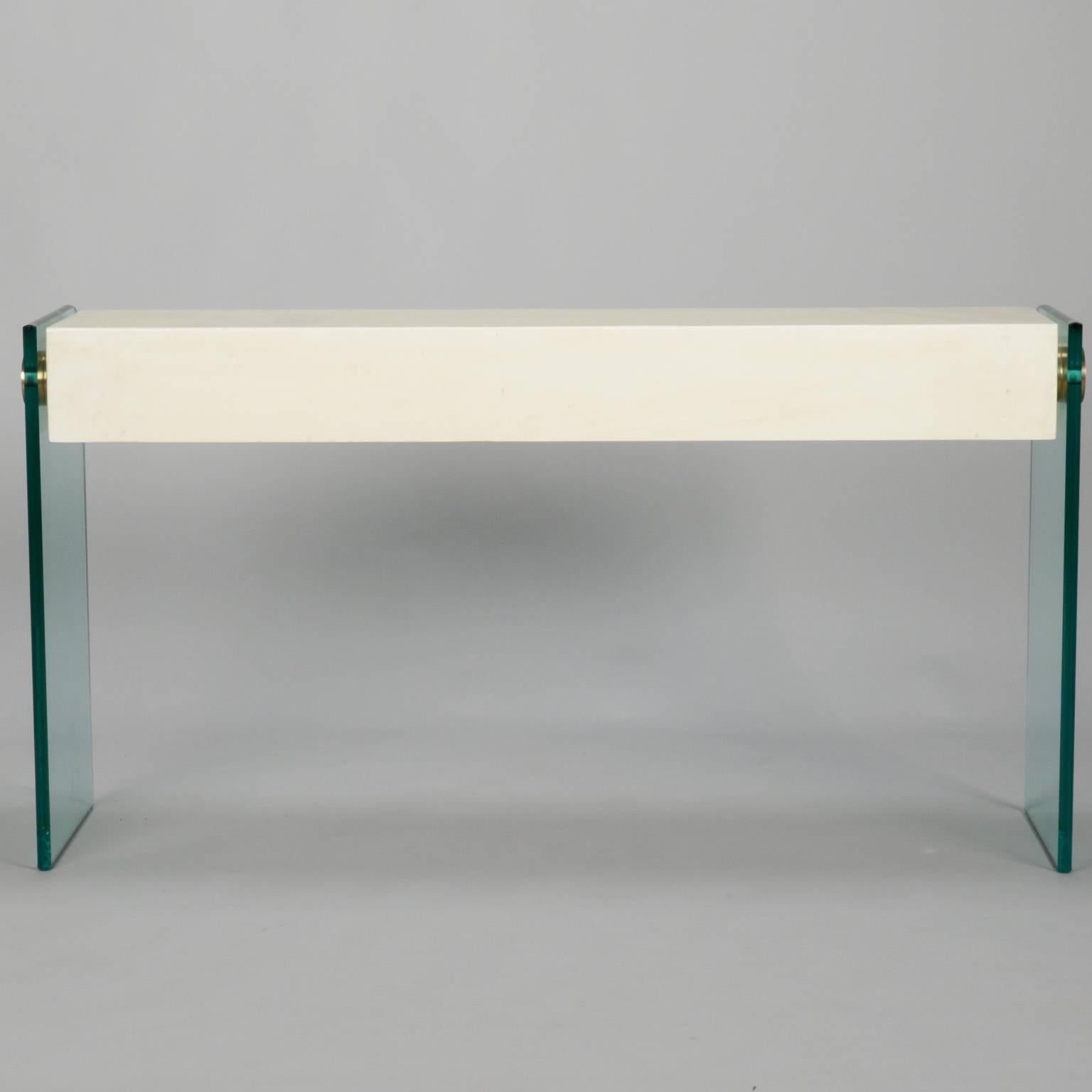 Circa late 1970s pair of modernist style consoles have wood table tops completely covered in bone tiles supported by heavy glass sides/legs and brass disk connectors. Bone tiles form smooth, curved edges and surfaces and have a thick, clear