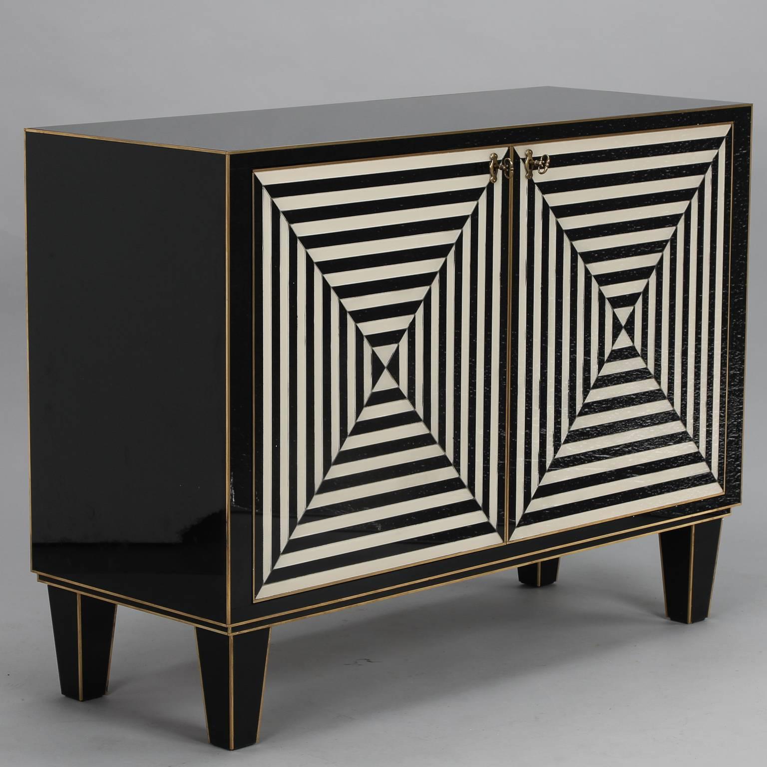 This Italian cabinet was made by a company in Padova, Italy in the late 1970s for a luxury hotel in Venice, Italy. The cabinet has a wood base with black and white Murano glass overlay panels and brass inlay and hardware. The front consists of two