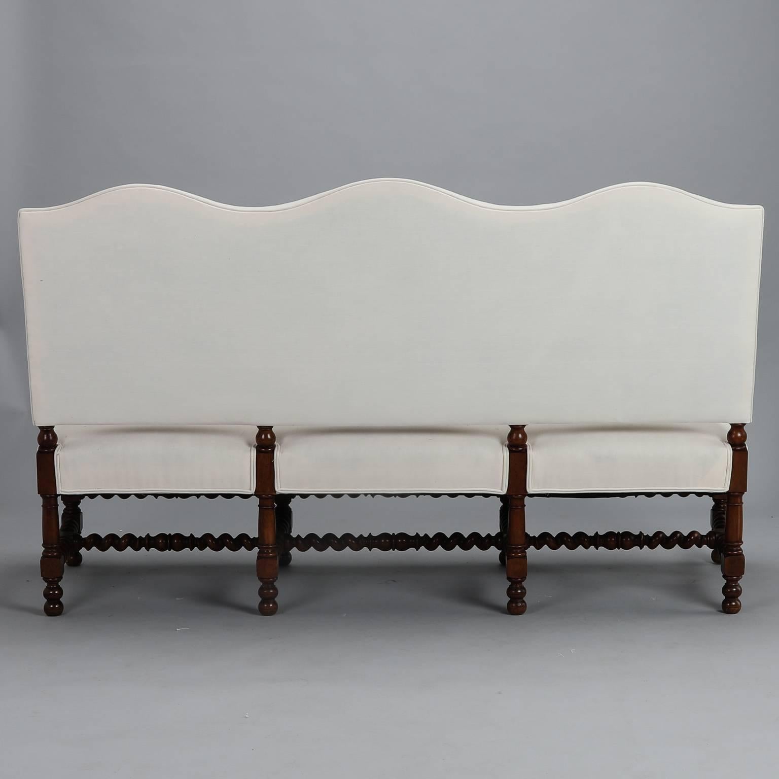 Late 19th century French camel back settee has a dark wood barley twist frame with double rail front stretcher, eight legs and upholstered arms. Newly covered in muslin, this piece is ready for the fabric of your choice. Arms are 27” high and seat