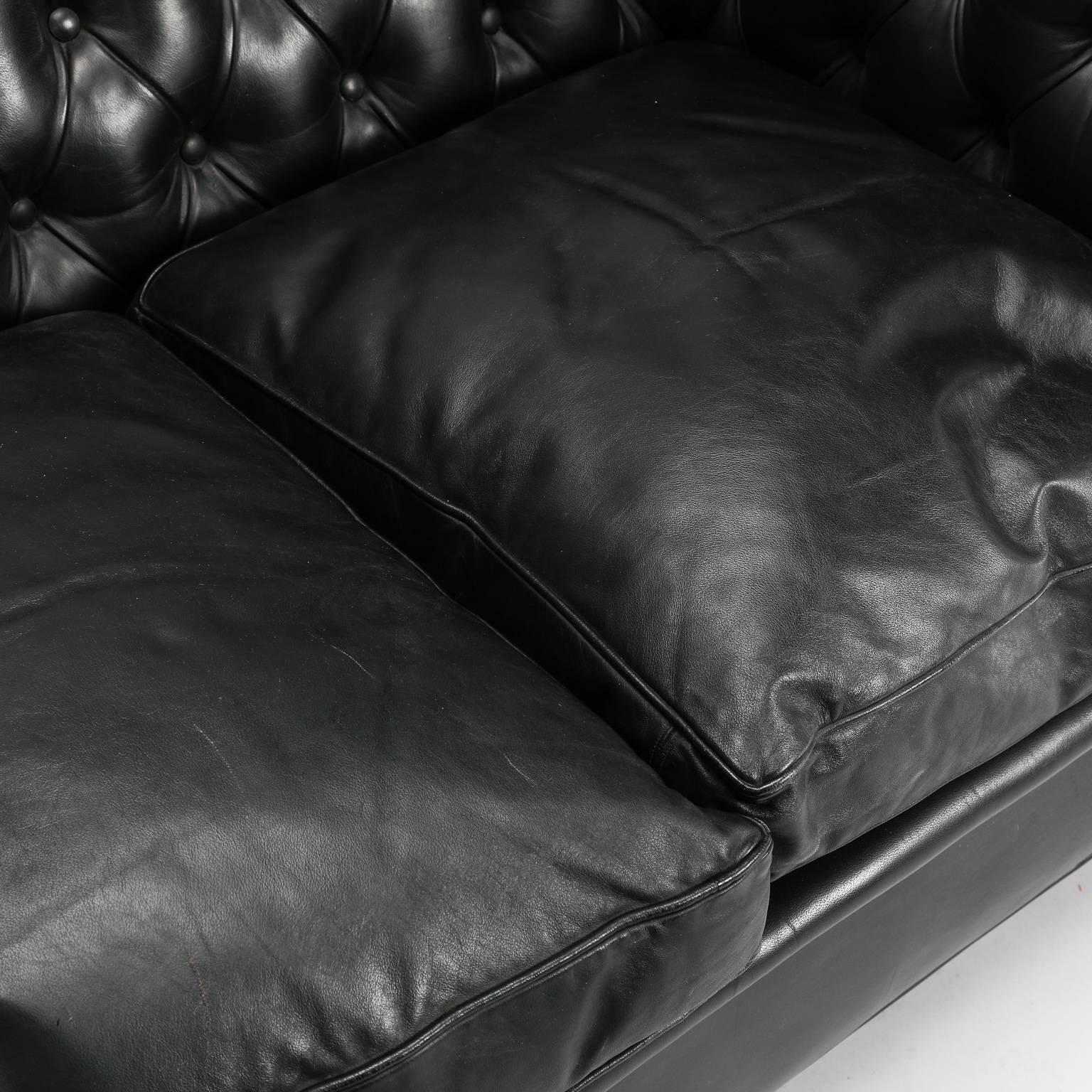 Three-seat black leather Chesterfield sofa found in England, circa 1960s. Rolled arms and backrest are diamond tufted with three separate seat cushions. Turned wood legs. Overall very good vintage condition with some wear to leather. Arms are 27”