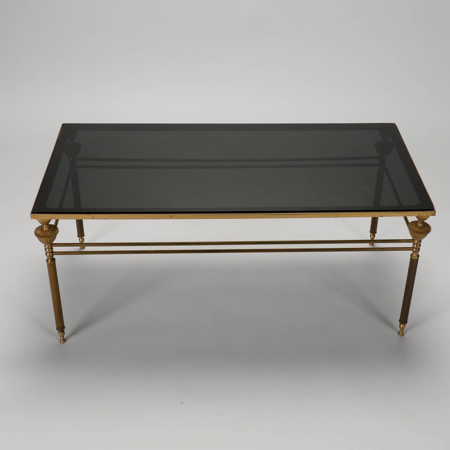 Brass framed French coffee table with smoke tinted glass table top, circa 1940s. Brass frame has classic French details and double rod stretchers. 
 