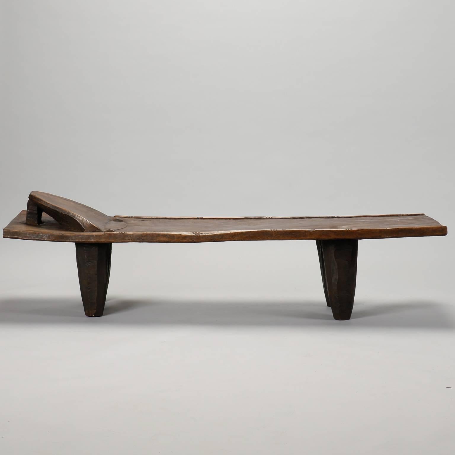 Wooden bench or daybed by the Senufo people of the Ivory Coast, circa 1970s. Dark stained wood bench has a built in head rest and thick, tapered legs.