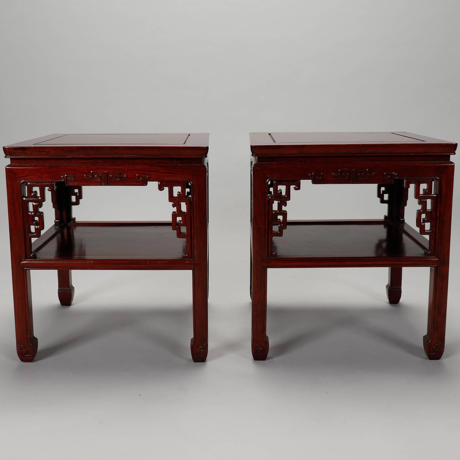 Pair of circa 1930s square Chinese wood side tables have lower shelf and decorative carved elements on the apron and corners. Unknown wood with red hued stain. Sold and priced as a pair. Other pieces from this set available at the time of this