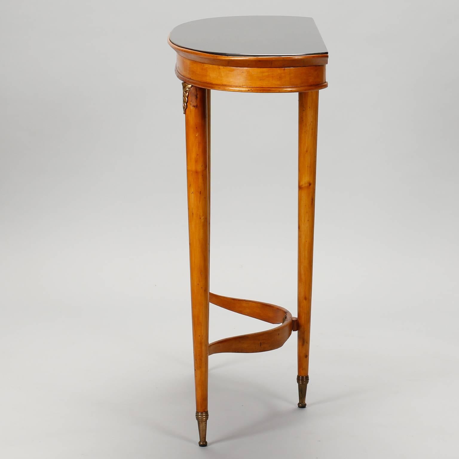 Found in France, this three-legged Art Deco era console has a demilune shaped top with black glass top, wood frame with three slender legs, curved stretcher and decorative brass fittings.
 