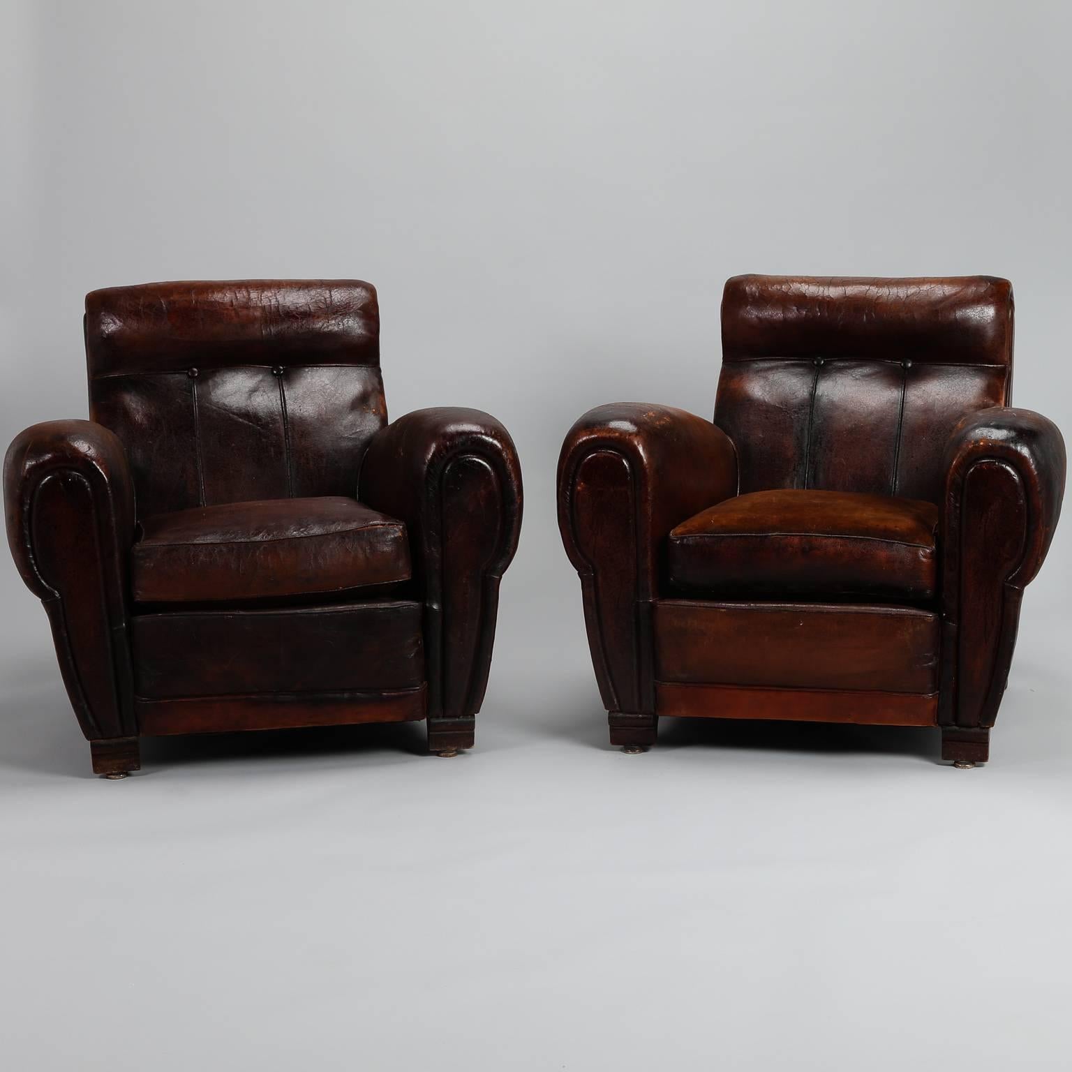 Pair of French club chairs in original dark brown leather, circa 1930s. Traditional, curvy form with button tufted angled seat backs, rolled arms and cushions with leather on one side and velvet on the other, decorative brass nailhead