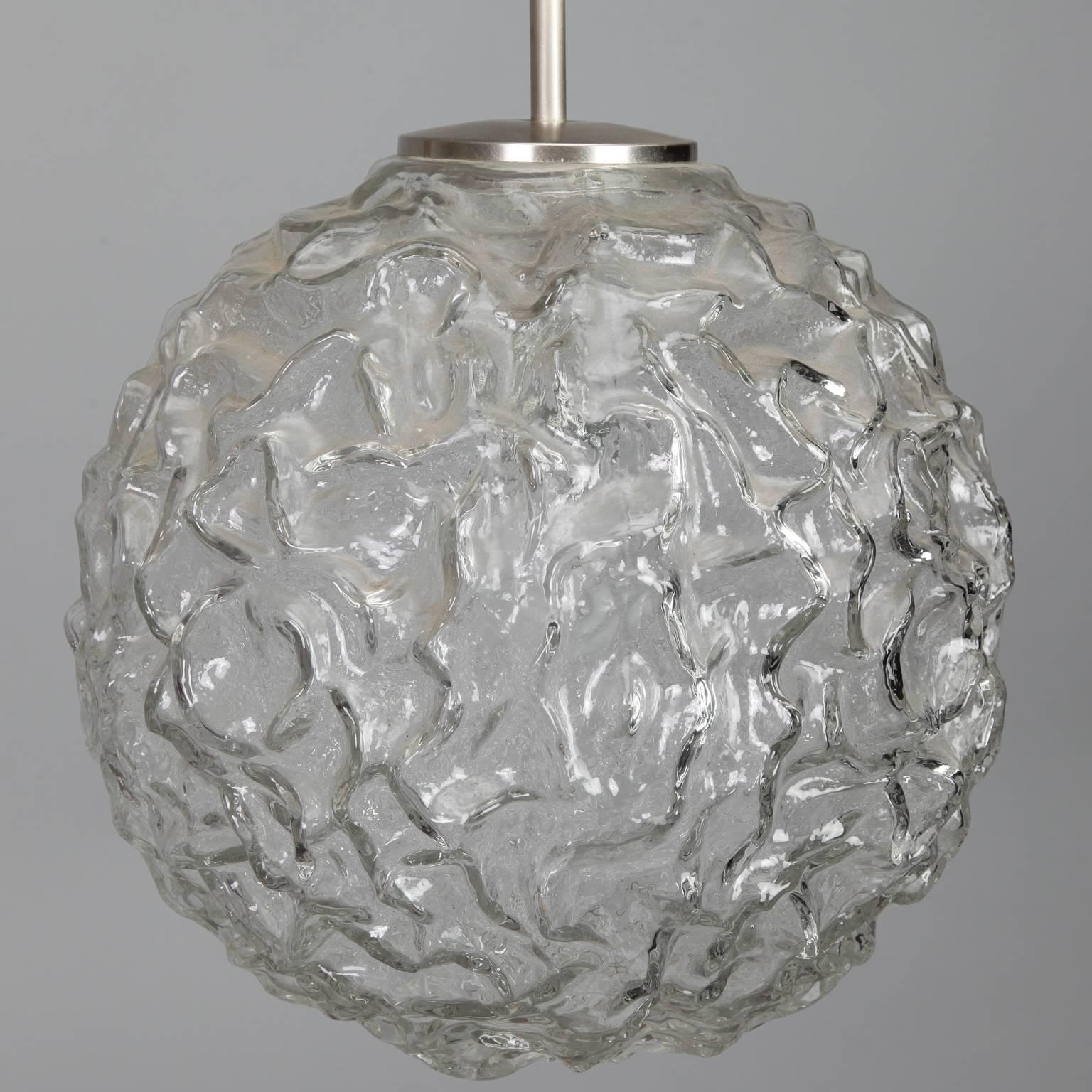 Globe shaped pendant fixture of thick, clear molded glass with a wavy surface texture. Polished nickel cylinder canopy and adjustable electrical cord, circa 1970s. New wiring for US electrical standards.