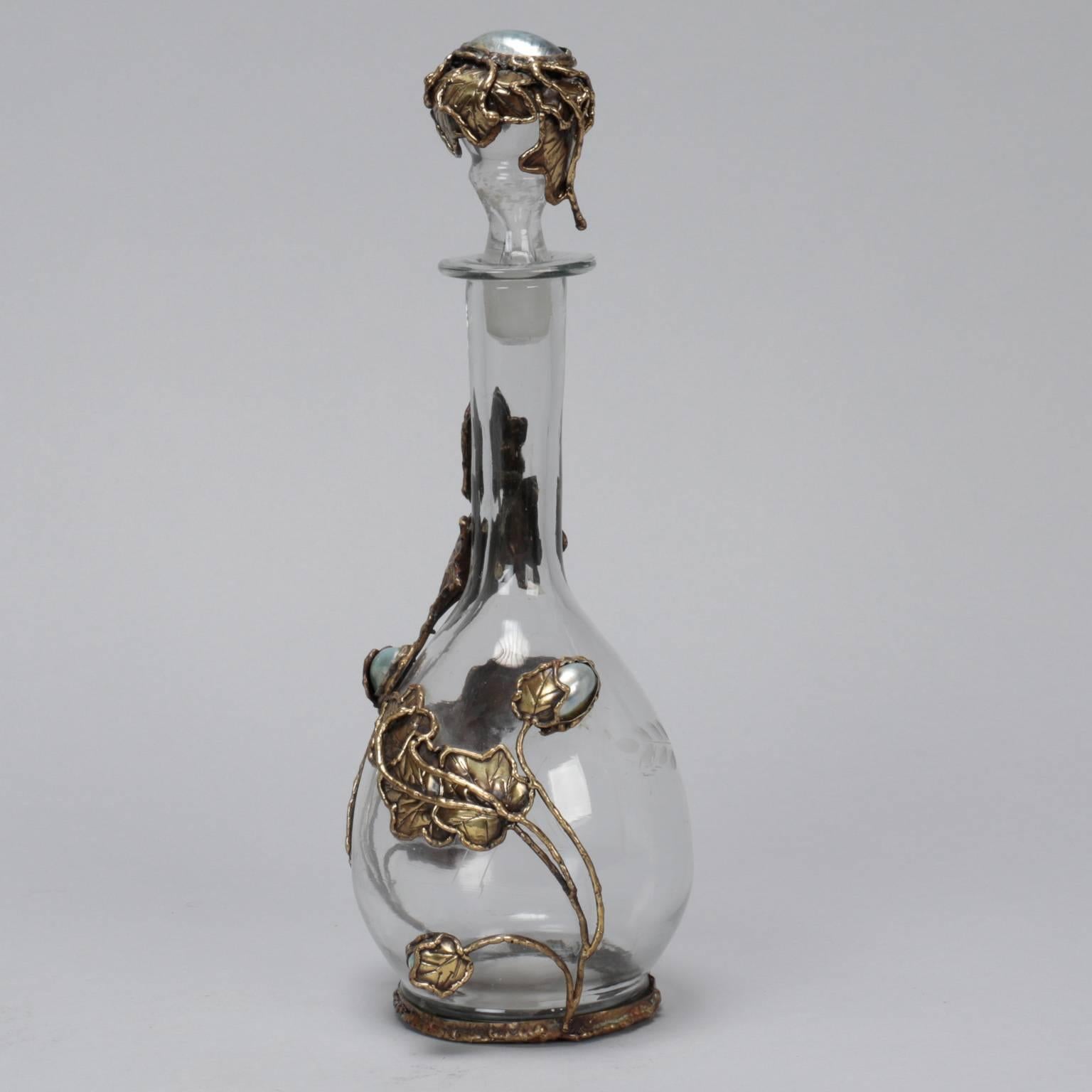 Found in Italy, this clear glass decanter has hand-forged brass toned metal leafy vines that wraparound the bottle and fresh water pearl accents. Signed by Lionel. Other pieces by this artist also available. Please inquire.
