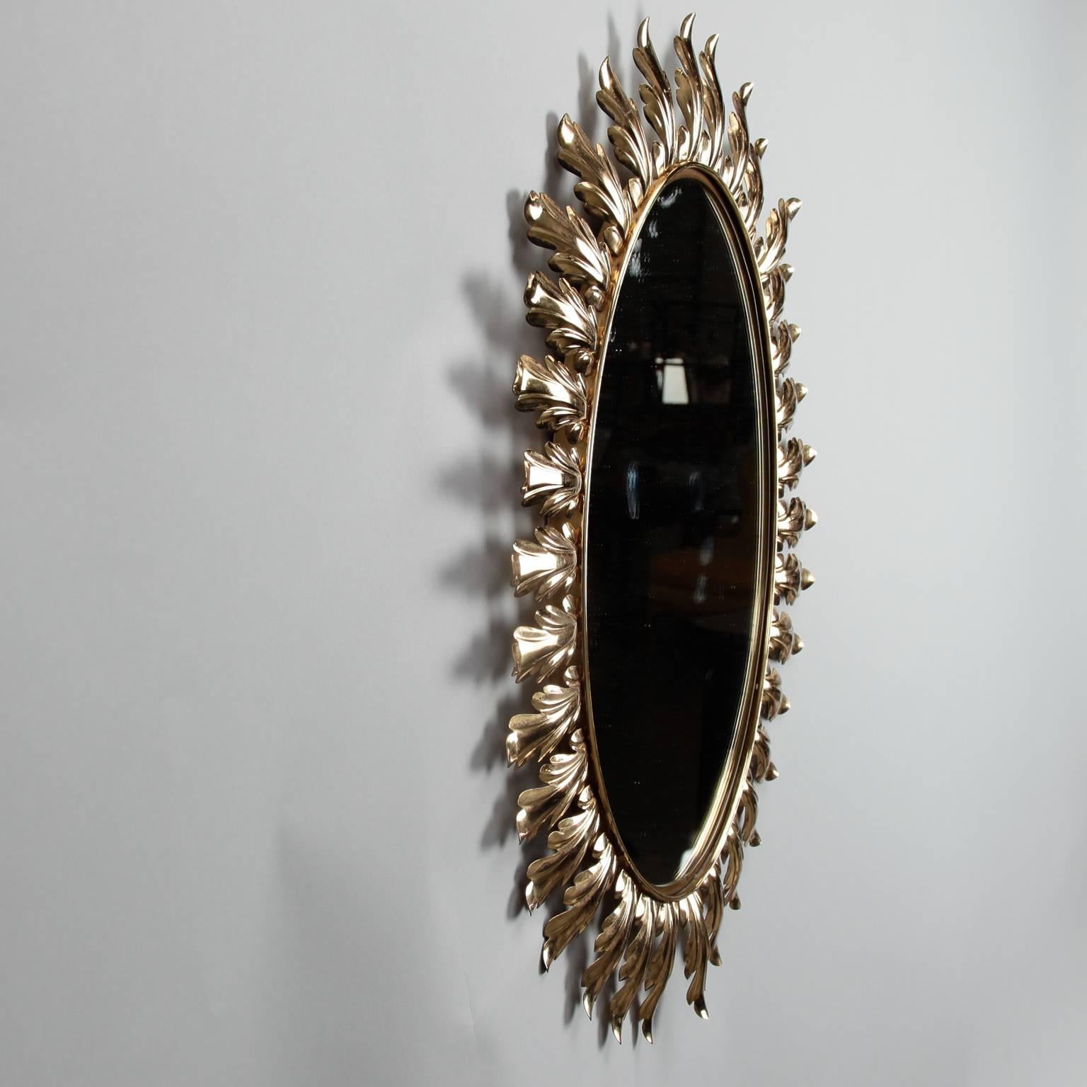 Italian oval mirror has a gold tone metal frame with acanthus leaf sunburst pattern, circa 1960s.