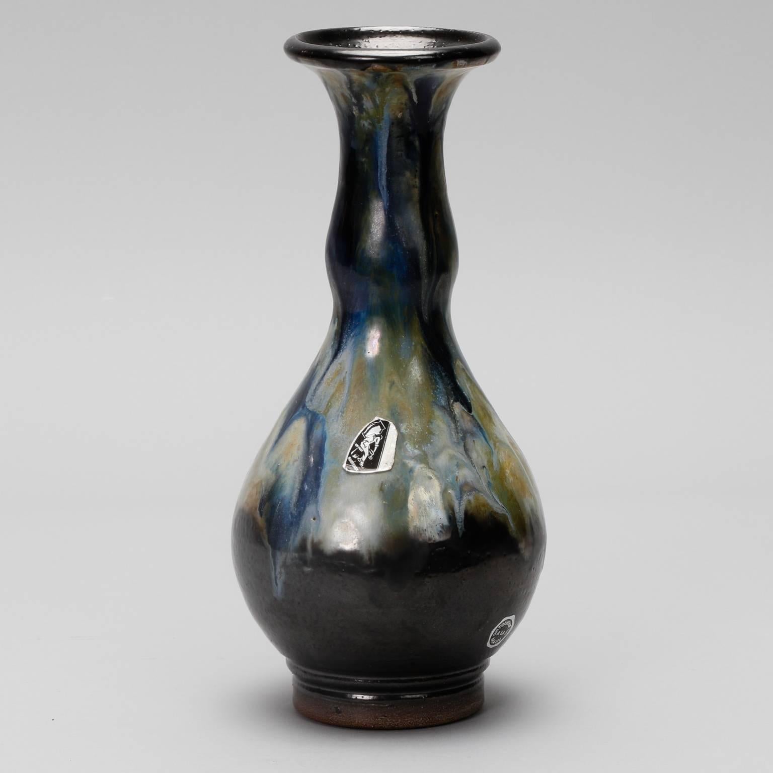 Slender vase signed by reknown Belgian ceramic artist Roger Guerin, circa 1930s. Mottled drip glaze in shades of blue, ochre and black. Original label still affixed.
