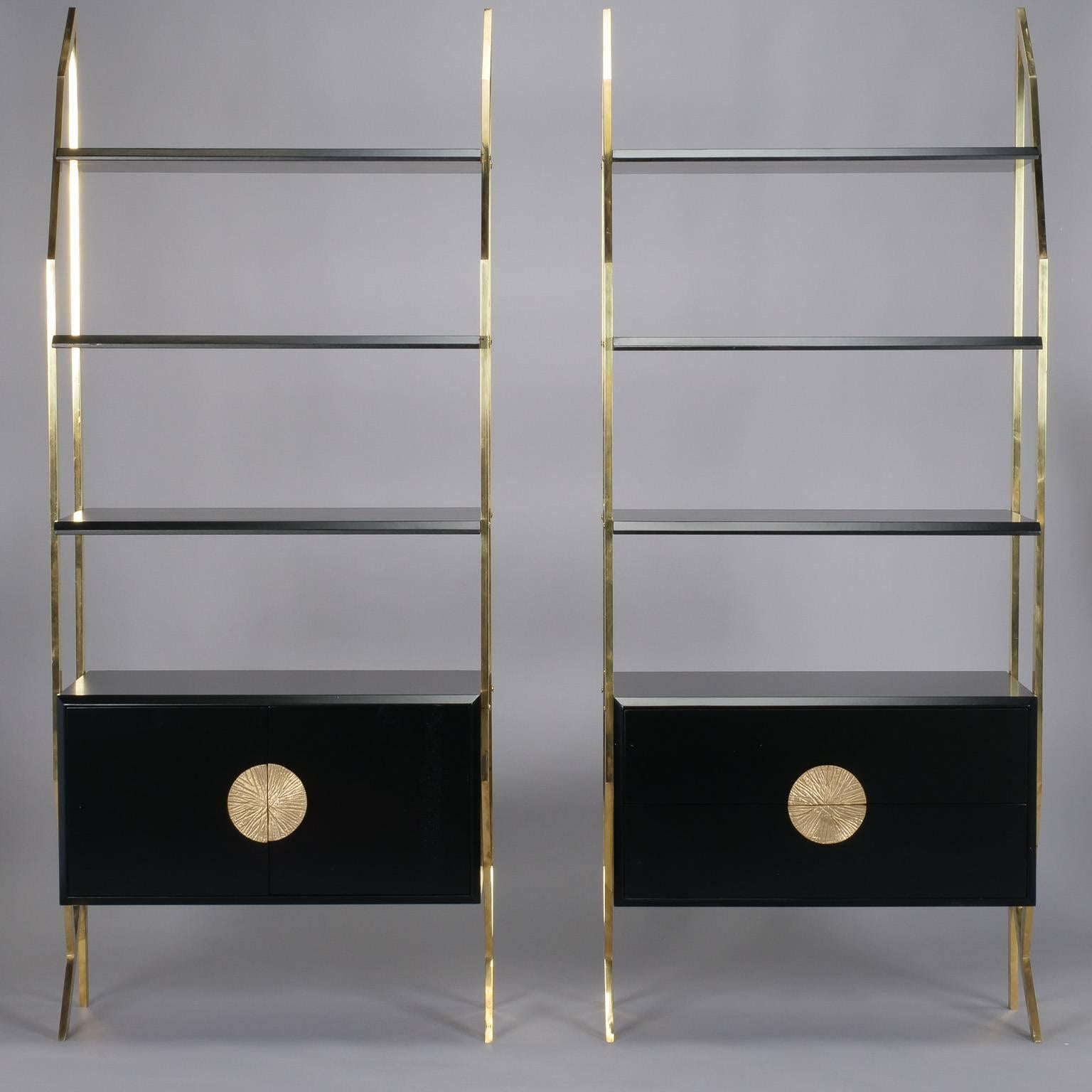 Pair of brass frame etageres with black enamel lower cabinets topped with three glass shelves, circa 1980s. Molded brass hardware. One cabinet has two drawers, the other has hinged door with open compartment. Clear glass shelves. Unknown maker. Sold