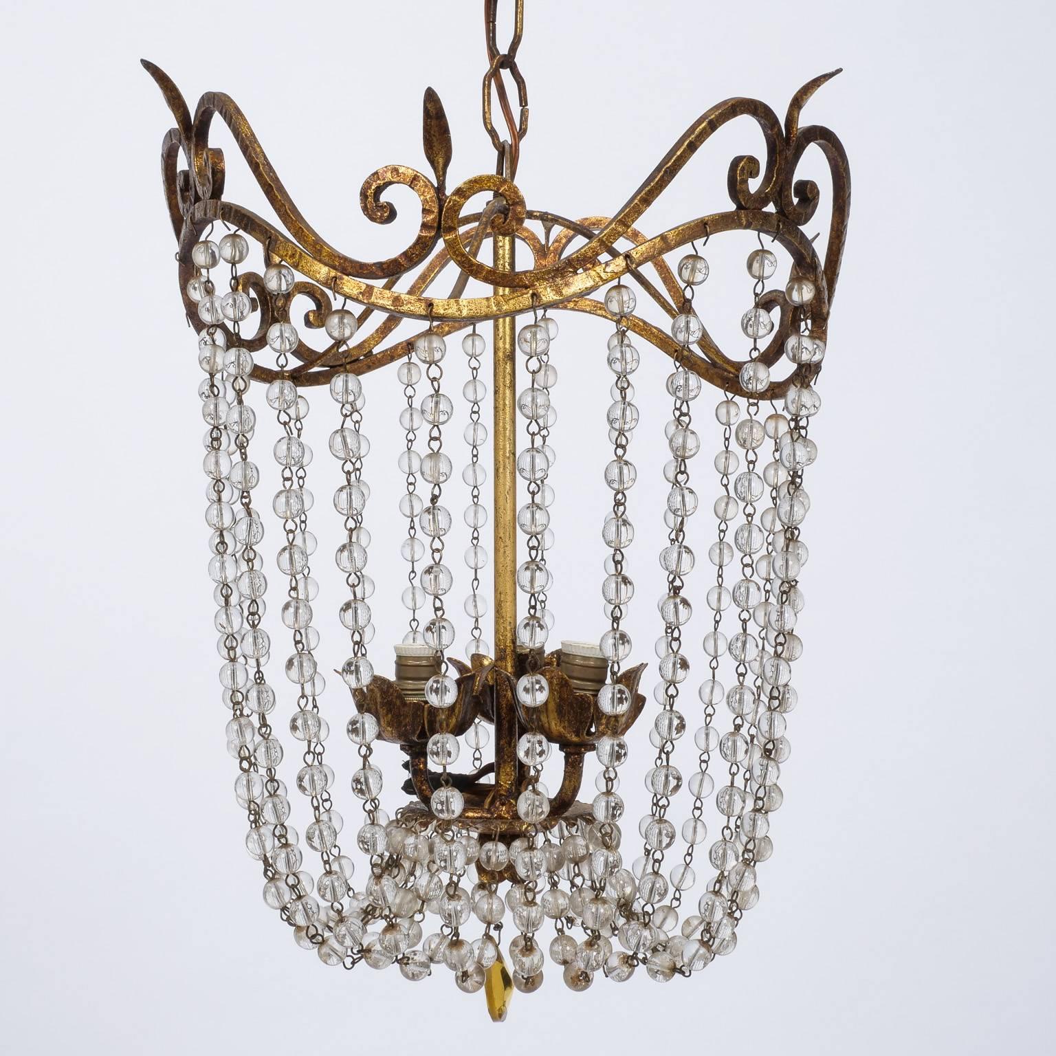 Era Empire style chandelier features a gilded iron frame draped with clear crystal beads, three internal candelabra size sockets and a pale amber faceted crystal drop. Subtle and elegant, this piece would work well in a powder room or bedroom.