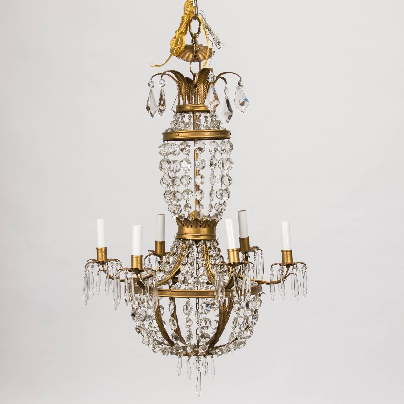 French Empire style chandelier has a double vessel form frame of gilt metal, circa 1920s. The lower level features strands of crystal beading draped in a globe form circled by a ring of six candle style lights with crystal accented bobeches. The