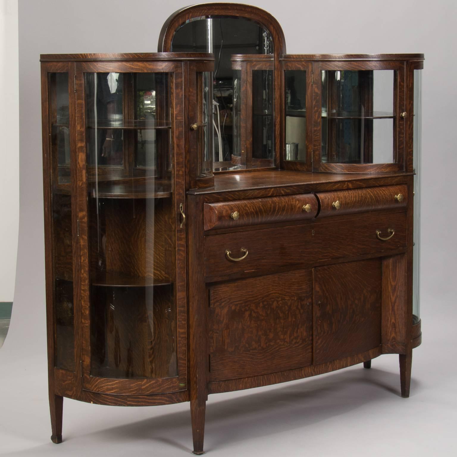 Quarter sawn oak cabinet flanked with two curved glass displays, circa 1900-1905. Centre arched and bevelled mirror, two centre curved front drawers over a single, deeper drawer and lower storage with two doors. Missing original keys (cabinets are