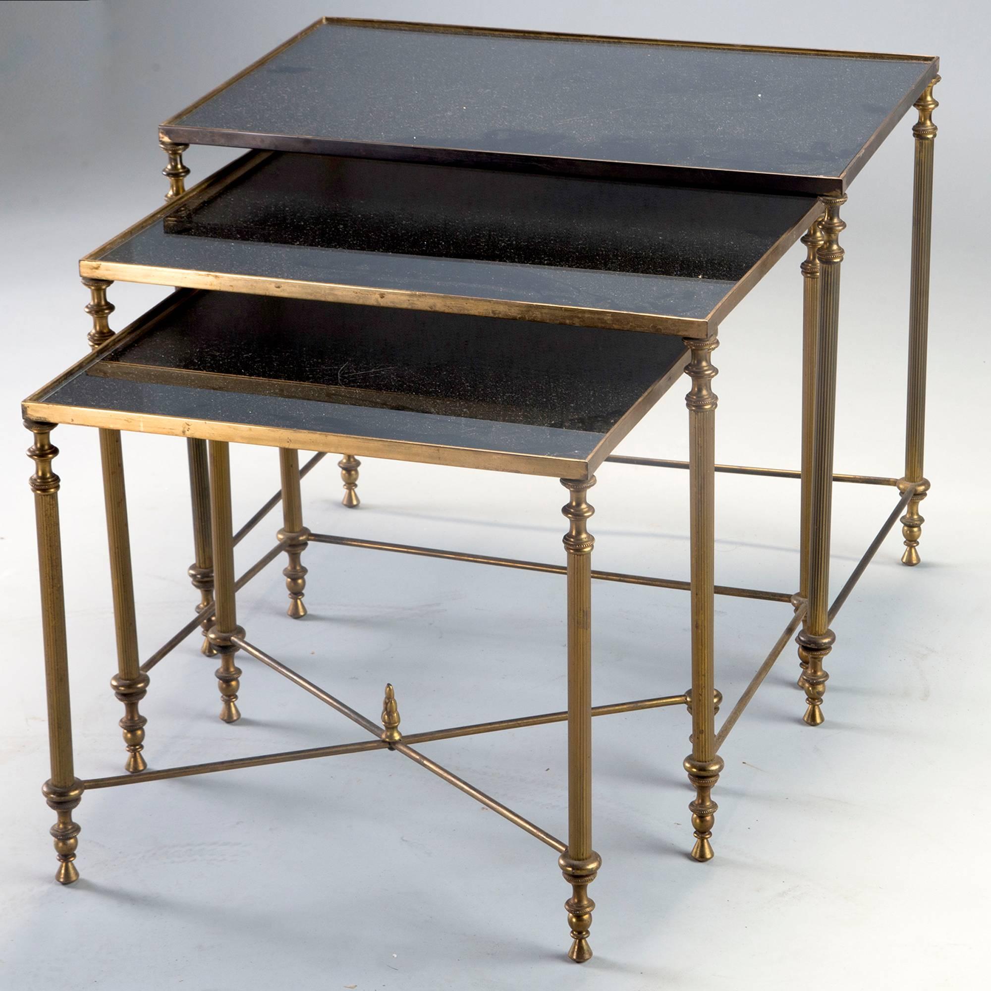 Three circa 1950s nesting tables with brass frames and black mirrored glass tops. Details include reeded legs with tapered feet and a criss cross stretcher with finial detail on smallest table. Measurements shown are for the largest table. Other