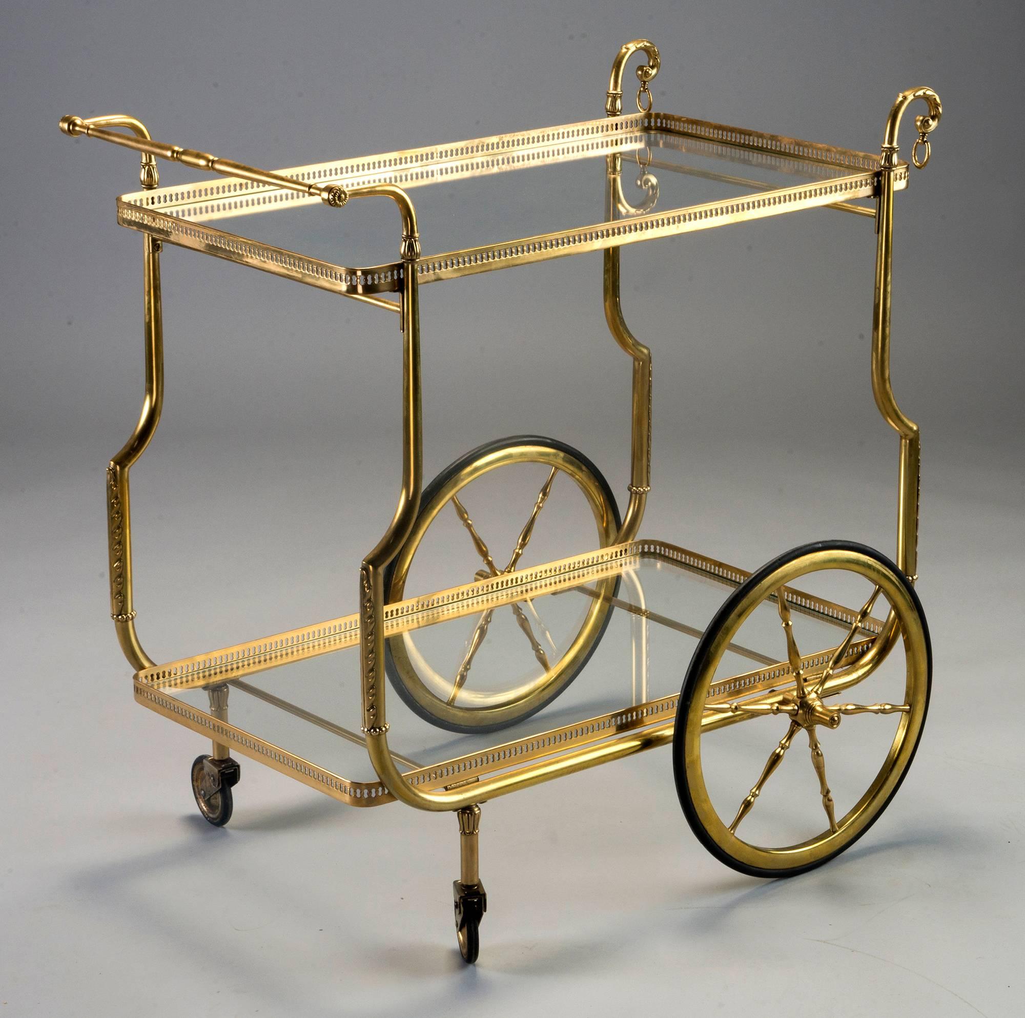Brass frame trolley has two clear glass shelves with open work brass galleries, circa 1930s. Tray form shelves are not removable. Leaf form embellishments on lower supports of frame, decorative spokes on large wheels. Unknown maker. Found in France.
