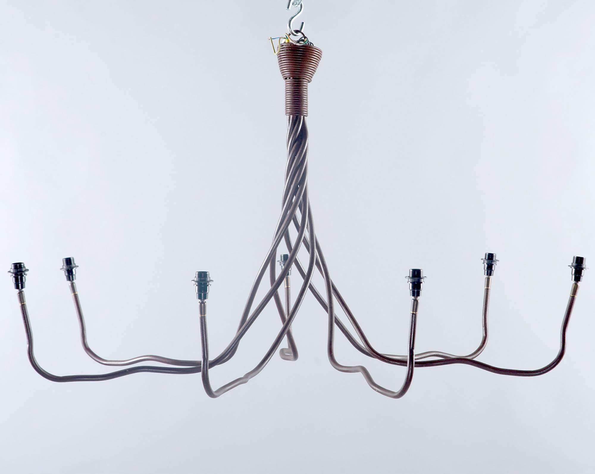 Il lampadario in ferro battuto è stato trovato in Belgio, intorno agli anni Settanta. La parte superiore dell'apparecchio presenta sette fili di ferro attorcigliati insieme e che si aprono gradualmente per formare i bracci del lampadario. Sette