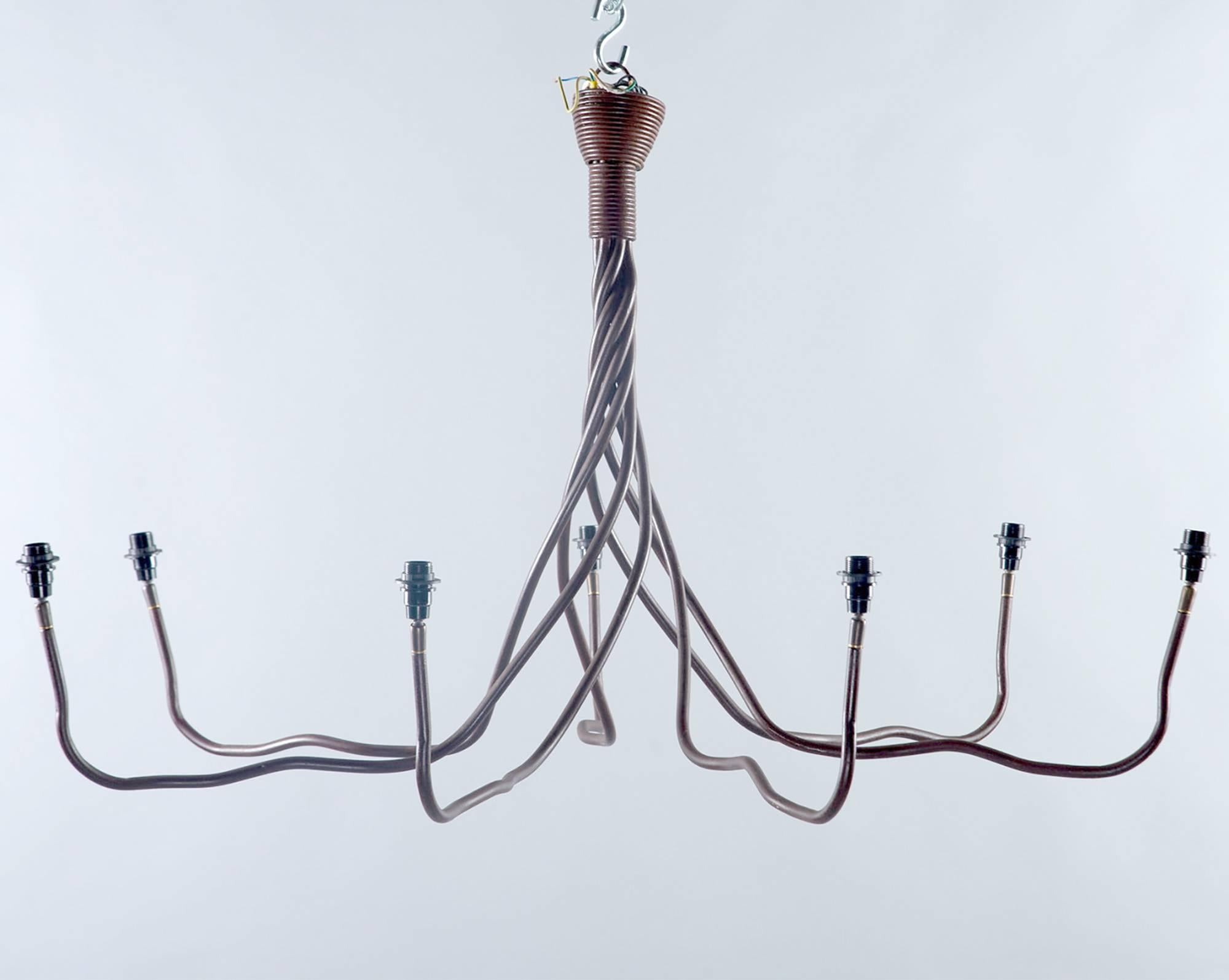 Wrought iron chandelier was found in Belgium, circa 1970s. Top of fixture has seven iron strands twisted tightly together and gradually opening to form the chandelier arms. Seven arms / candelabra size light sockets in total with white cloth shades.