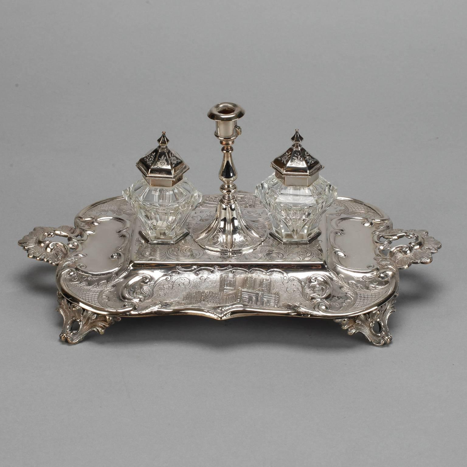 Found in England, this silver plated ink well set includes a silver plated tray with decorative handles and feet, two clear cut glass inkwells with silver plated tops and a coordinating silver plate candlestick. Sold and priced as a four piece set.