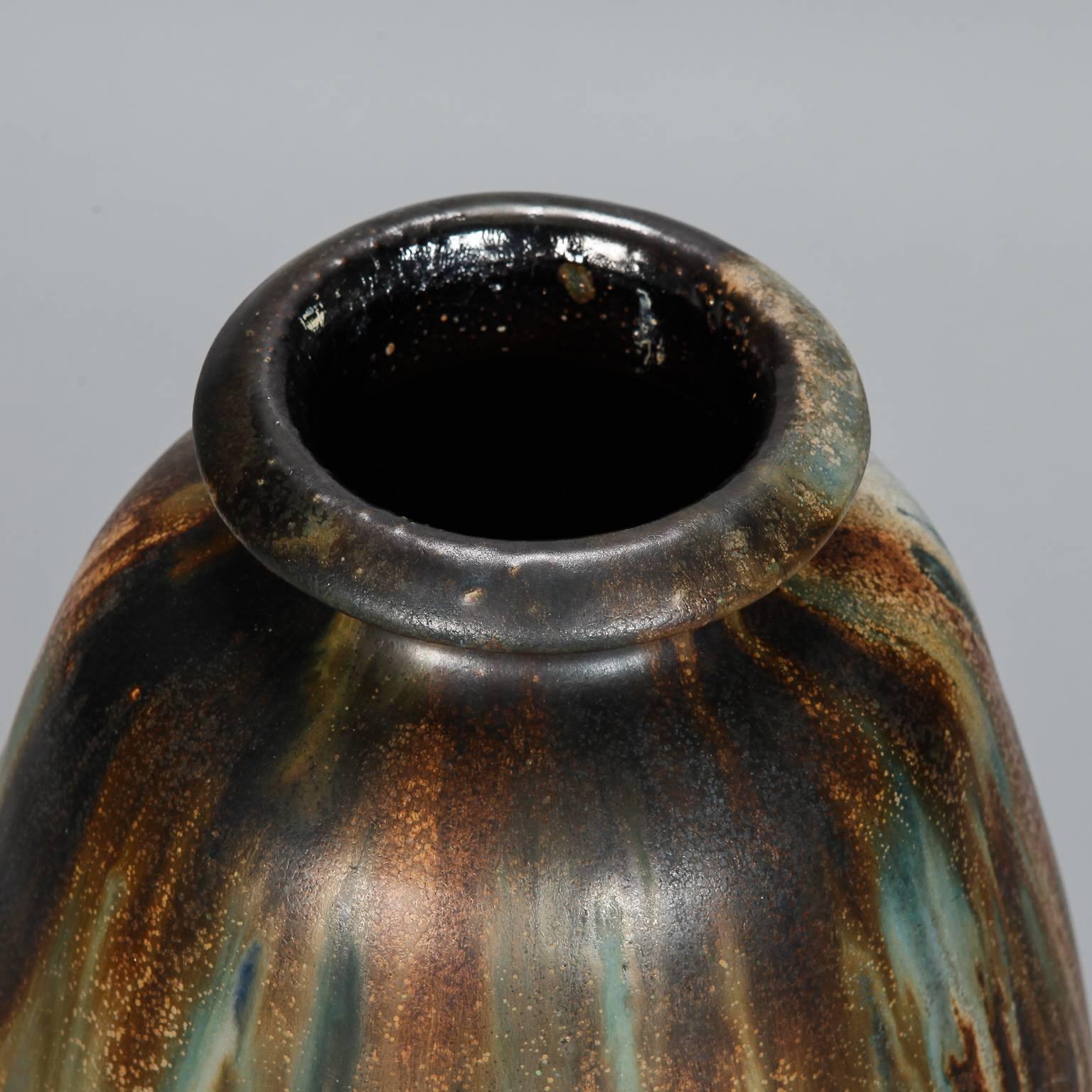Circa 1930s tall vase signed by famed Belgian ceramic artist Roger Guerin is just under 2 feet tall. Classic shape with narrow neck and rim in distinctive, streaky glaze with gold, blue, rust and earth tones. Artist signature incised on bottom.
