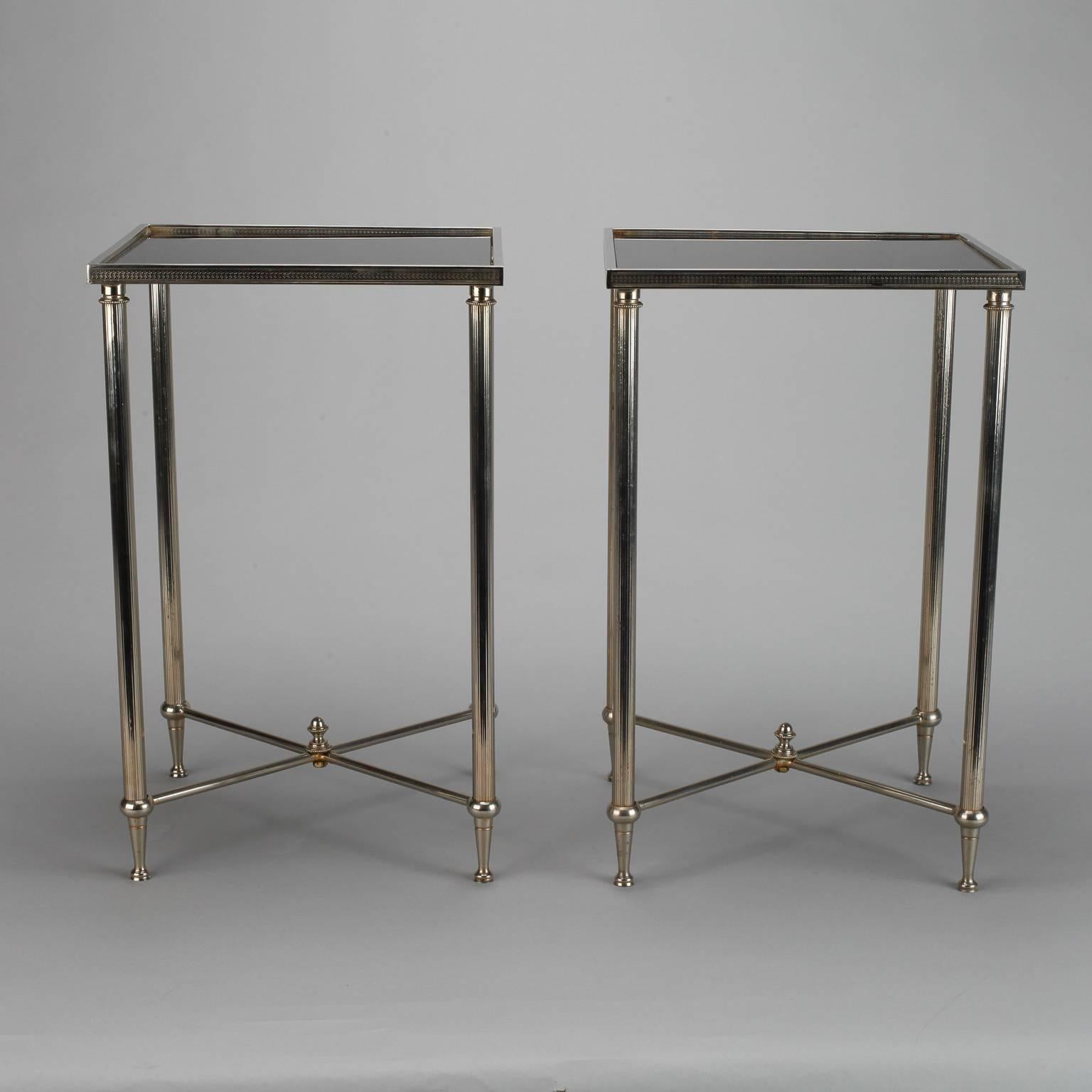 Pair of circa 1960s small square accent tables found in France feature classically styled details including silver tone finish, reeded legs, and criss-cross X-form stretchers topped with finials. Table tops are black glass. Sold and priced as a pair.