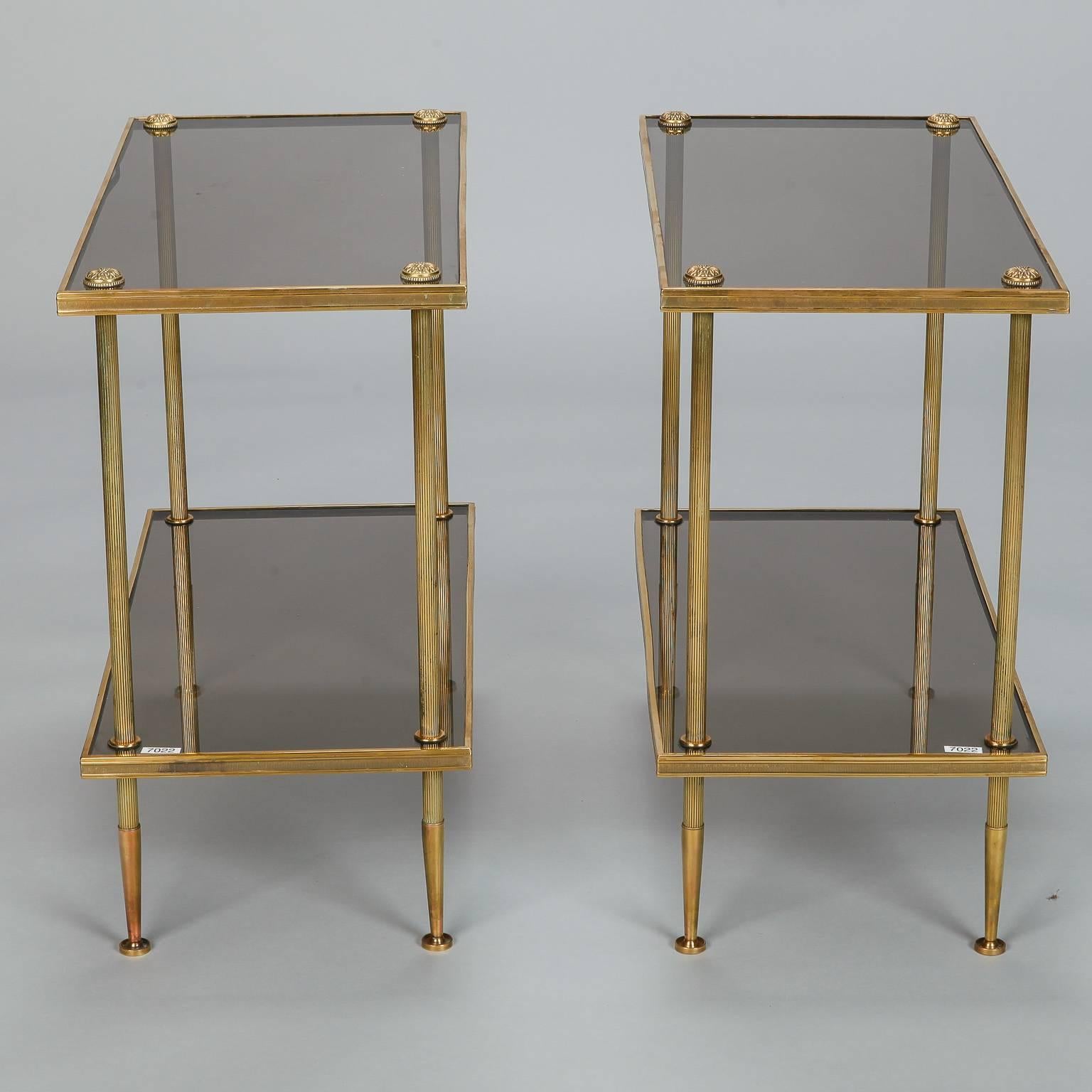 Pair mid century two tier tables by Jacques Quinet dating from the 1960s. Brass frames have reeded, tapered legs, decorative hardware and smoked glass shelves. Sold and priced as a pair. 

Dimensions:
21.5” H x 24” W x 12” D

Retail:
$4,295.00