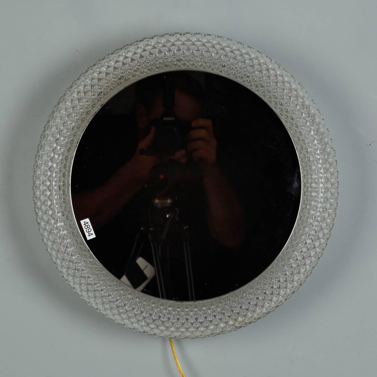 Round mirror light probably originates from Germany, circa 1970s. Clear textured glass floating style frame with round mirror that has a light at the back. New electrical wiring for US standards.  Actual Mirror Size:  12.5” diameter

 