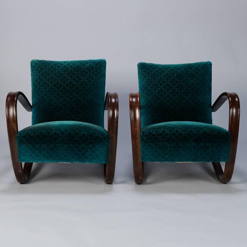 Circa 1930s Model H269 upholstered lounge chairs with distinctive curved arms and legs designed by Jindrich Halabala. Cut velvet in teal green appears original or is quite old and has visible signs of wear and age. Dark stained wood arms show wear