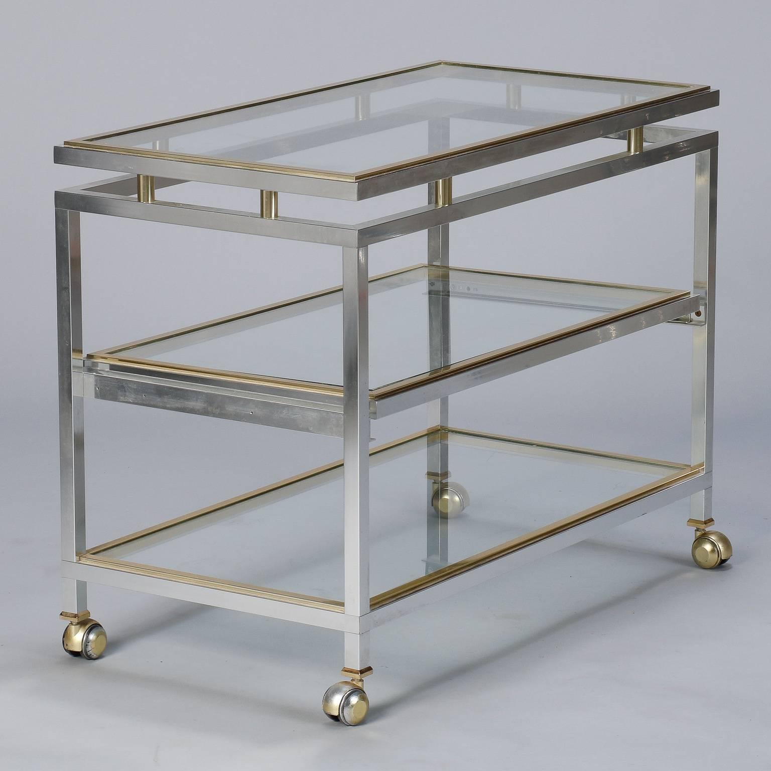 Found in France, this circa 1970s serving cart / trolley has a brushed chrome frame with contrasting brass trim and clear glass shelves. Middle shelf slides out. Style similar to pieces designed at the time by Maison Jansen but no manufacturer’s