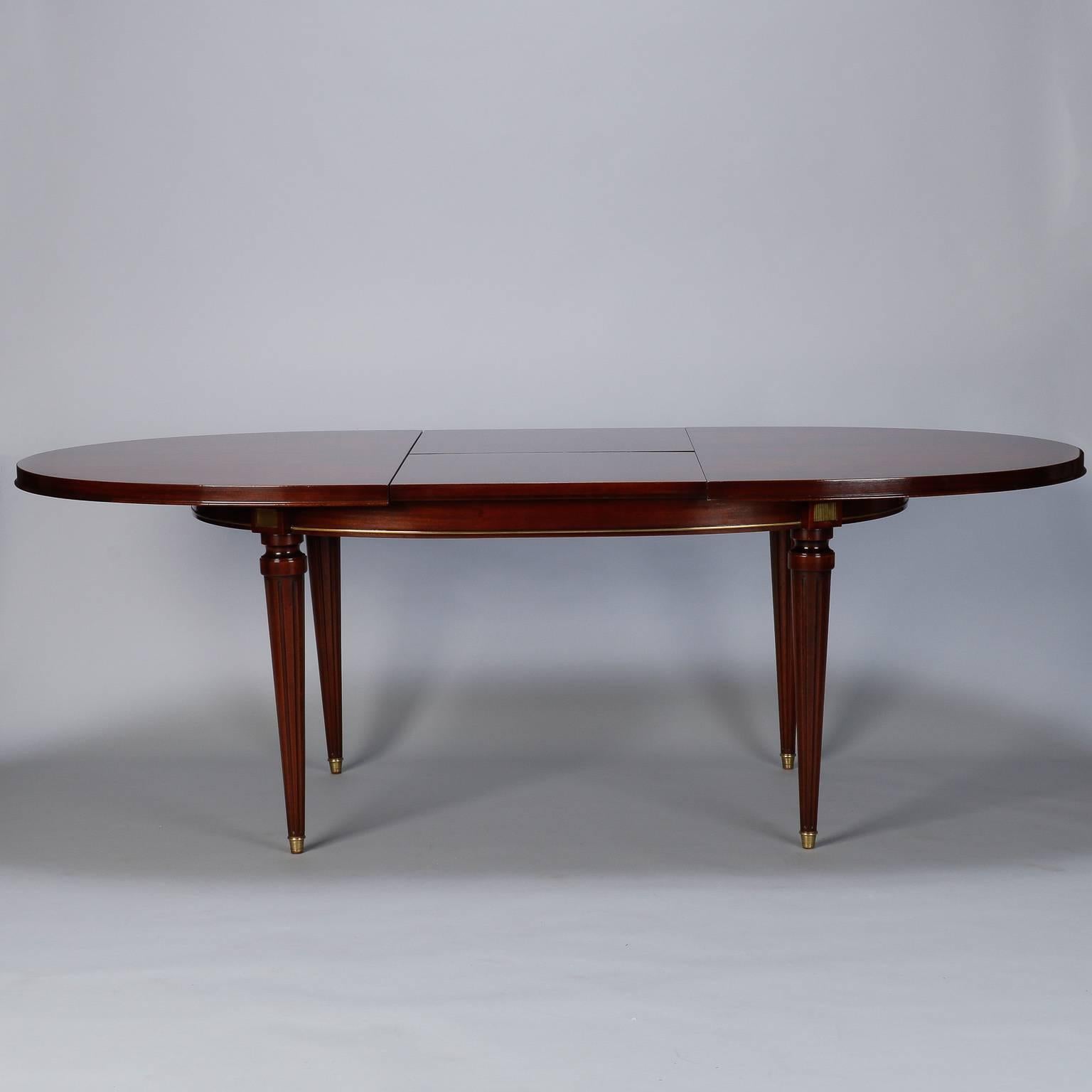Circa 1930s French oval dining table in classic Louis Philippe style. Dark, richy grained mahogany with beautifully bookmarked top and self-storing butterfly leaf of 24” wide. Reeded and tapered legs have brass mounts at the base and brass capped
