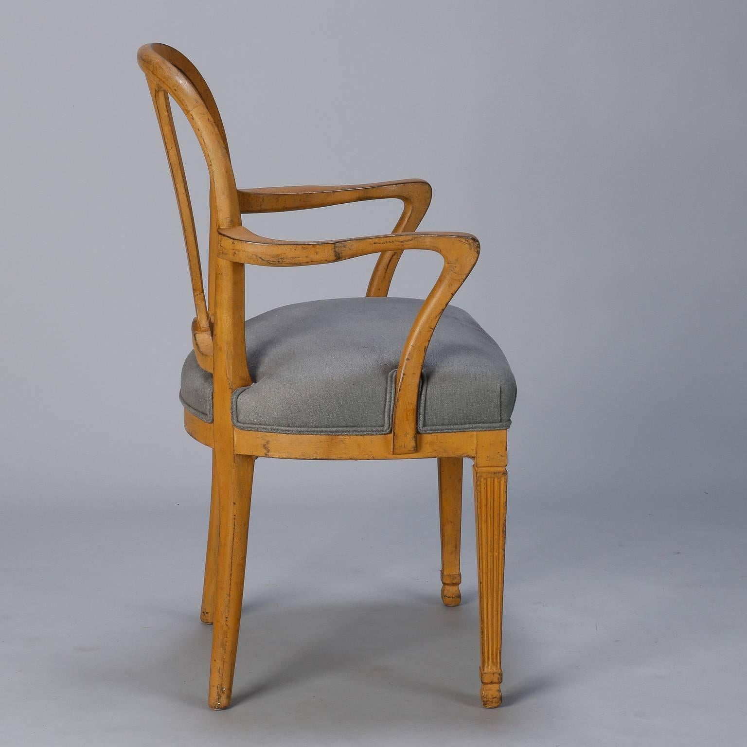 Circa 1920s French arm chair has rounded back rest with flared, urn shaped splat and curved arms. Reeded front legs, and flared back legs. Muted rusty orange brown painted and distressed finish with newly upholstered seat in blue gray fabric. Arms