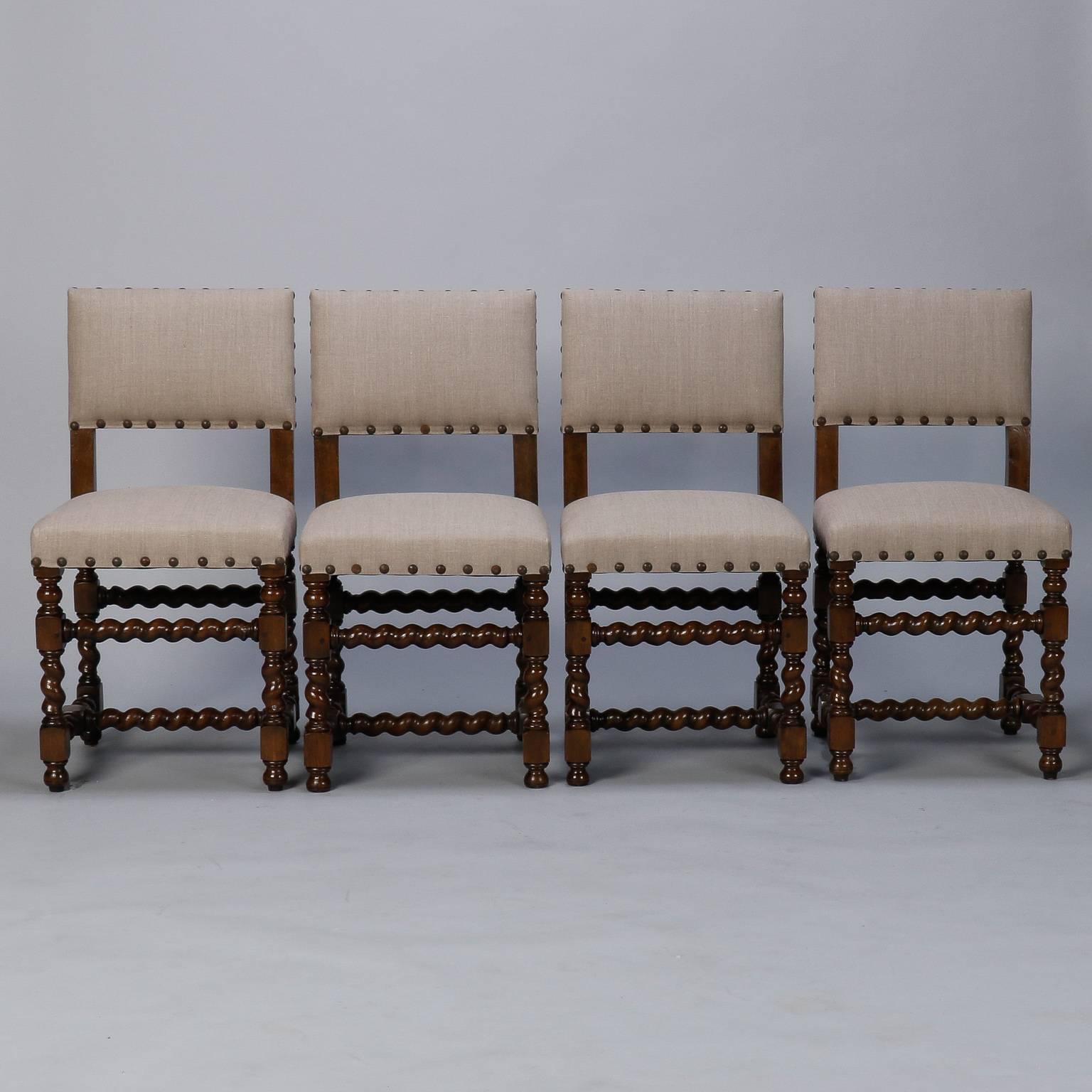 Circa 1920s set of six Spanish dining chairs with carved barley twist legs, arms and stretchers. Two arm chairs with padded arms and four side chairs. All are newly upholstered in natural colored linen and accented with oversize decorative brass