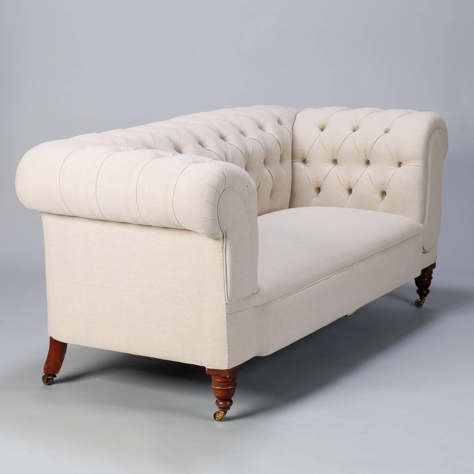 English Chesterfield sofa has been reupholstered in natural colored linen fabric, circa 1920s. Diamond tufting on inside and top of backrest and inside of rolled arms. One arm has a hinge release lever on the side that lowers the arm and allows the