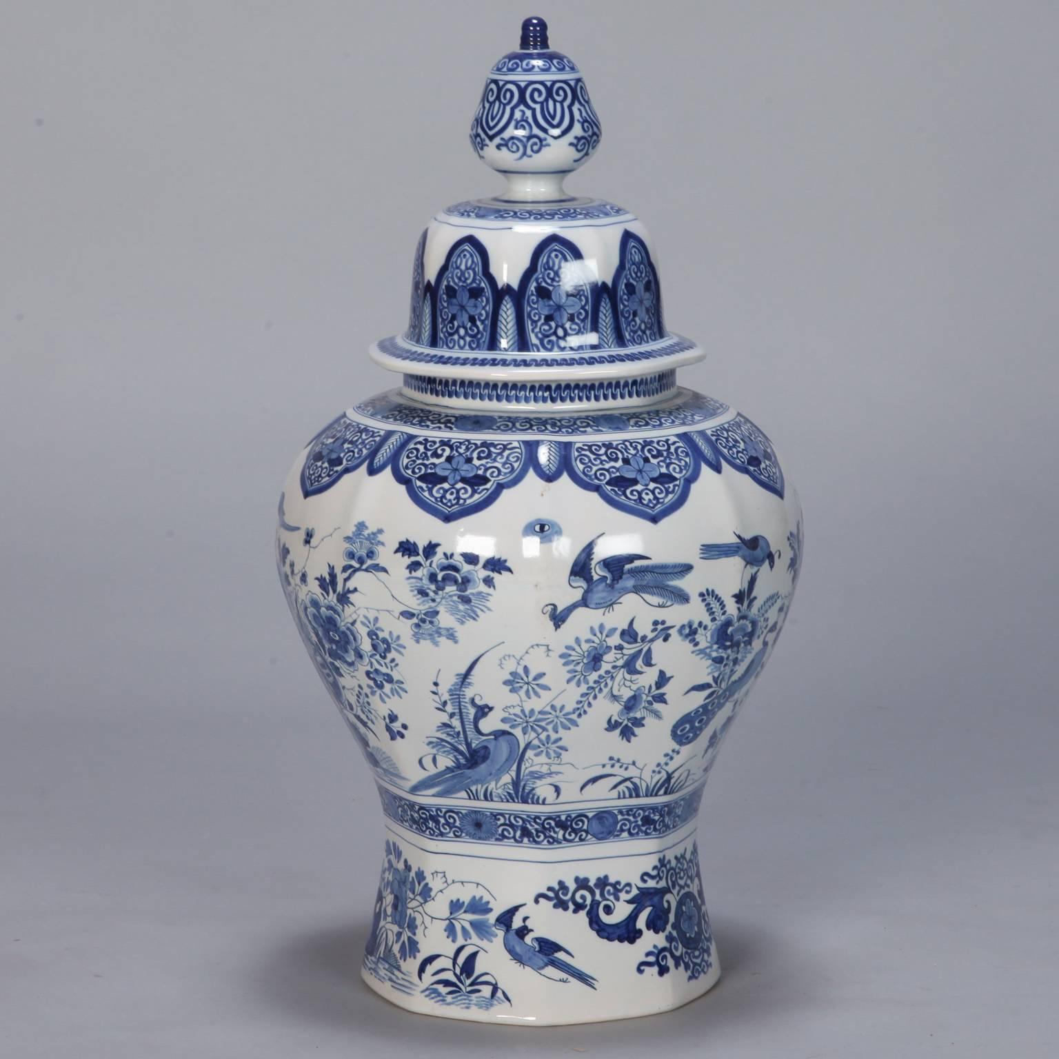 Large early 20th century Dutch vase in Classic blue and white glaze depicts peacocks, flowers, butterflies and decorative borders at the neck and lid. Body of vessel is subtly paneled and with the lid in place, this piece is two feet tall.
 