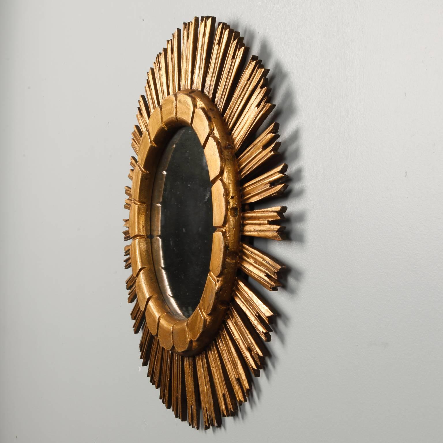 Giltwood mirror in sunburst form has rays with jagged tips and an incised scallop design on the inner frame, circa 1960s. Mirror has scattered black spots all-over but frame is in excellent condition.   Actual Mirror Size:  10” diameter

 