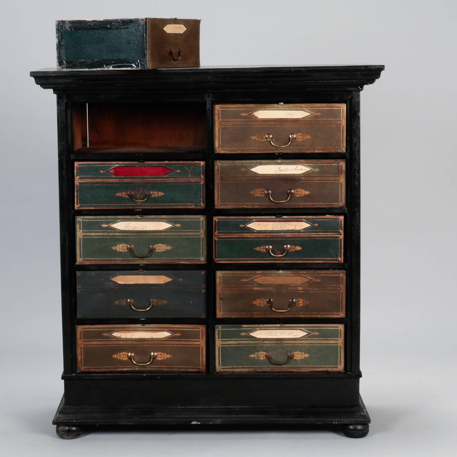 Circa 1890s oak chest has an ebonized finish and ten removable suitcase style drawers. Drawers are made of heavy paperboard and covered in paper with leather fronts and brass hardware. Drawer fronts fold down and are secured with clip at top.