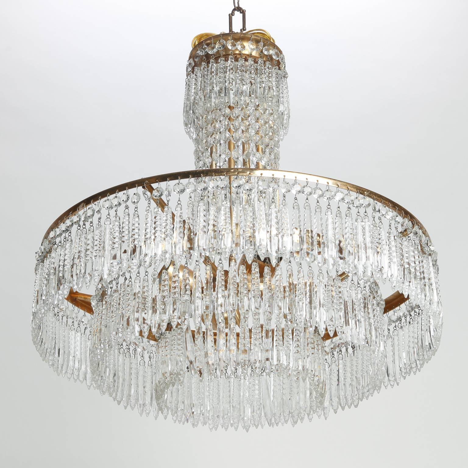 French chandelier features a brass frame with narrow center support decorated with crystal pendants and three graduated tiers of hand-cut crystal pendants. Four full size sockets and brass ceiling canopy. New wiring for US electrical standards,