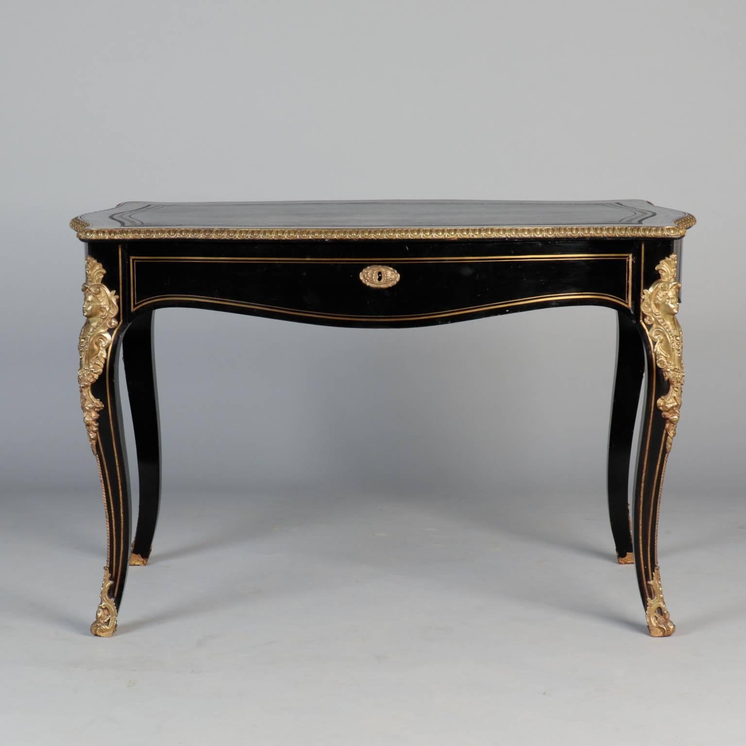 Regency style writing desk in ebonised finish with locking center drawer and leather top, circa 1880. This piece features classic French lines and elaborately detailed gilded ornamental female bust and foot cap on each leg. Curved apron with gilded
