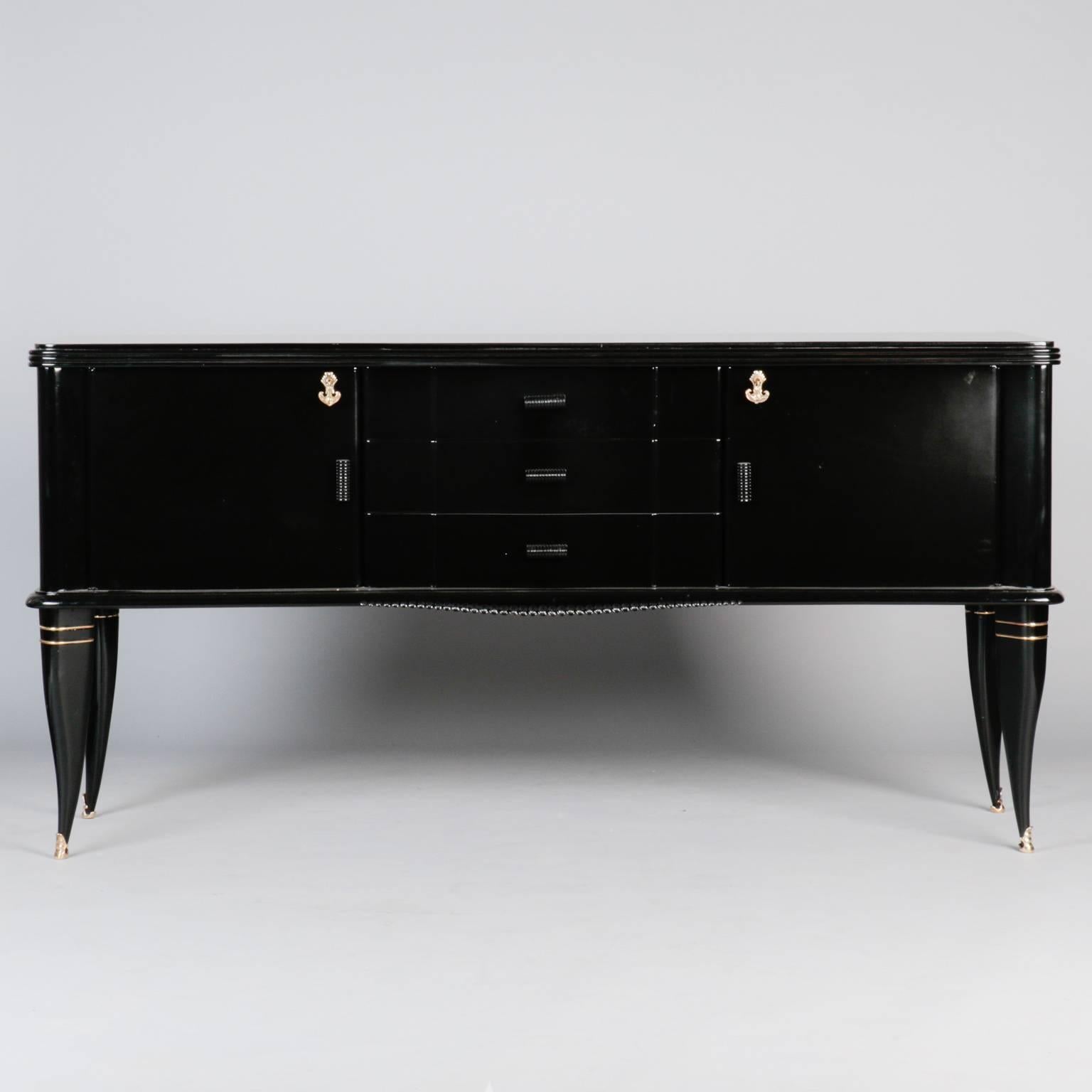 Side board with ebonized finish and brass accents, circa 1930s. Three center functional drawers flanked by side cabinets with hinged and locking doors. Curvy tapered legs with brass feet and accents. Very good vintage condition.