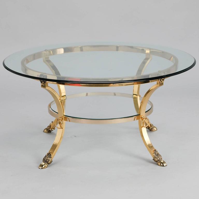 Brass base round cocktail table with glass top made by Spanish maker Almerich, circa 1980s. Cast and polished brass base has four legs with hooved feet and ram’s head decorations and a thick, clear glass top. At the time of this posting, we also