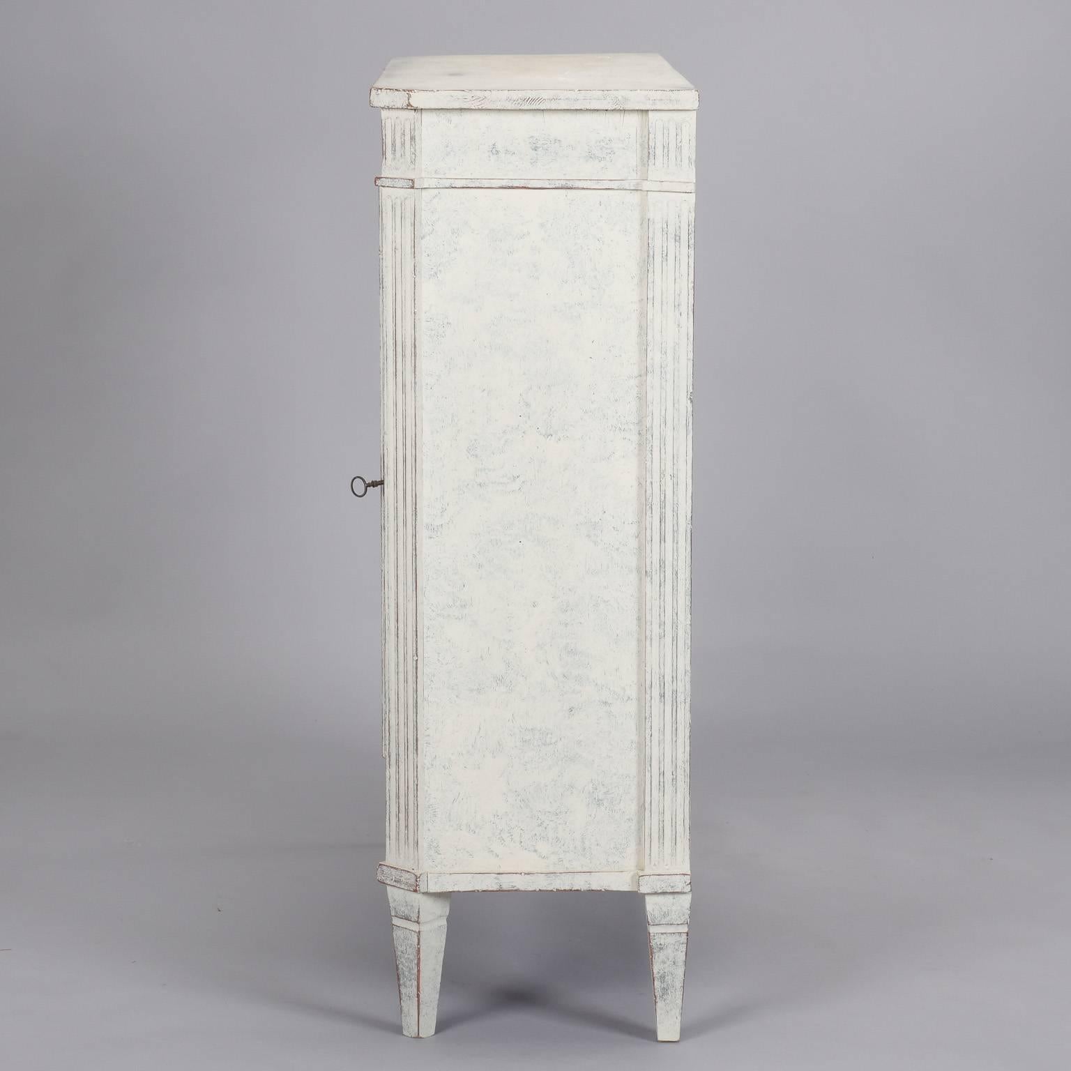 French shallow two-door cabinet has new side rails and painted finish in creamy white with blue gray undertones, circa 1900. Reeded legs, decorative carved details on apron and sides, working skeleton key. Two internal shelves.