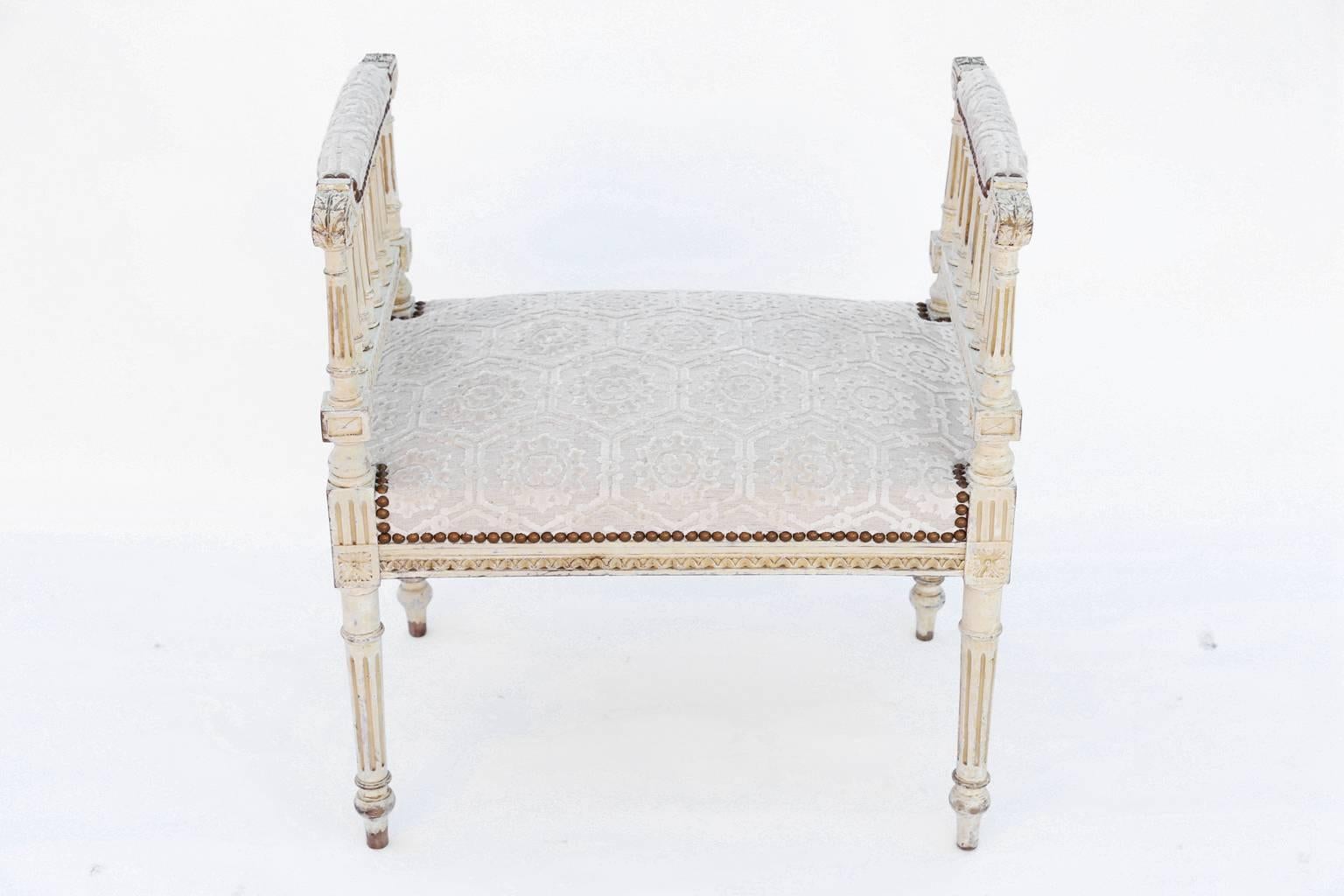 Window seat bench, in the Louis XVI style, having a painted finish with natural wear, its padded armrests ending in scrolls, raised on a balustrade arcade, its padded crown seat on a fielded apron carved with gadrooning, raised on round, fluted,