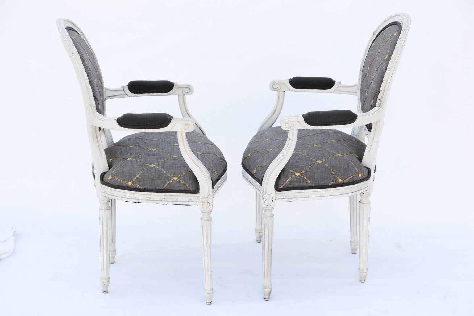 Pair of fauteuils, in the Louis XVI style, each having a white painted finish, showing natural wear, the oval fielded frame carved with gadrooning, surrounding its padded back, outswept, channelled arms with padded elbow rests, ending in scrolls, on