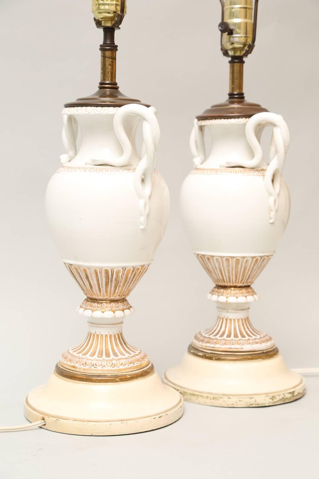 Pair of lamps, each a porcelain urn with gilt decoration, having entwined figural snake handles, lamped on later metal bases.

Stock ID D8209