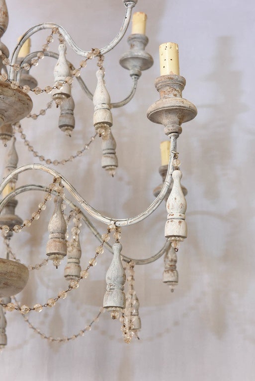 Unusual chandelier, having a distressed painted finish; its turned knopped centre column, with two tiers of six S-scroll candle arms of iron, terminating in flared wooden bobeches, each arm draped with strings of glass beads, and accented by wooden