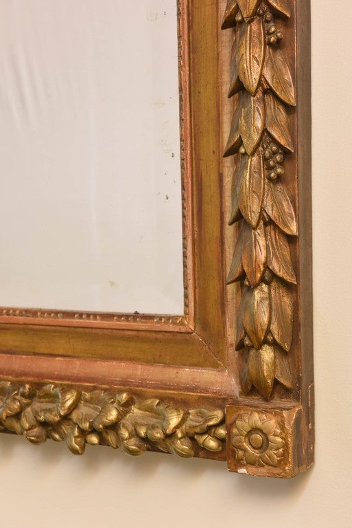Wall mirror, having a beveled rectangular mirror plate, in a giltwood frame, carved with laureling on one side, and with oak leaves on the other, divided by rosette-carved corner blocks, surmounted by pierced bow and ribbon cresting.