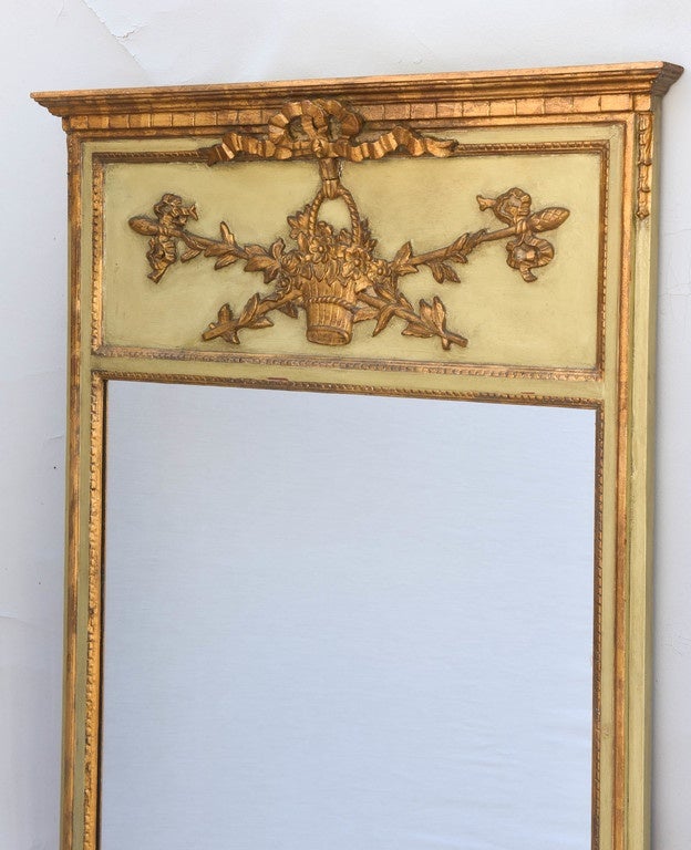 Pair of trumeau mirrors, painted and parcel gilt, each having a differently carved pediment; a musical motif with harp and horns, and floral basket with ribbons and rods, surmounting painted frame with beaded border.