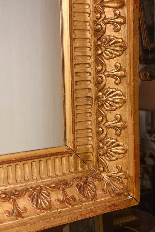 Mirror, having a rectangular mirror plate in carved giltwood frame, its molded border, surrounded by fluting, and framed in out-carved anthemion and scrollwork.