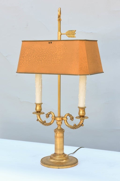 Single lamp, of gilt bronze, having double S-scroll candle arms ending in two lights, raised on round base with beading decoration, its rectangular tole shade, in orange, adjusts with arrow-form key, on its central post, finished by a ring